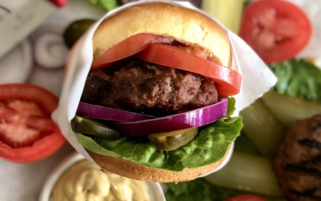 Hamburger fresh off the grill surrounded by juicy and fresh toppings