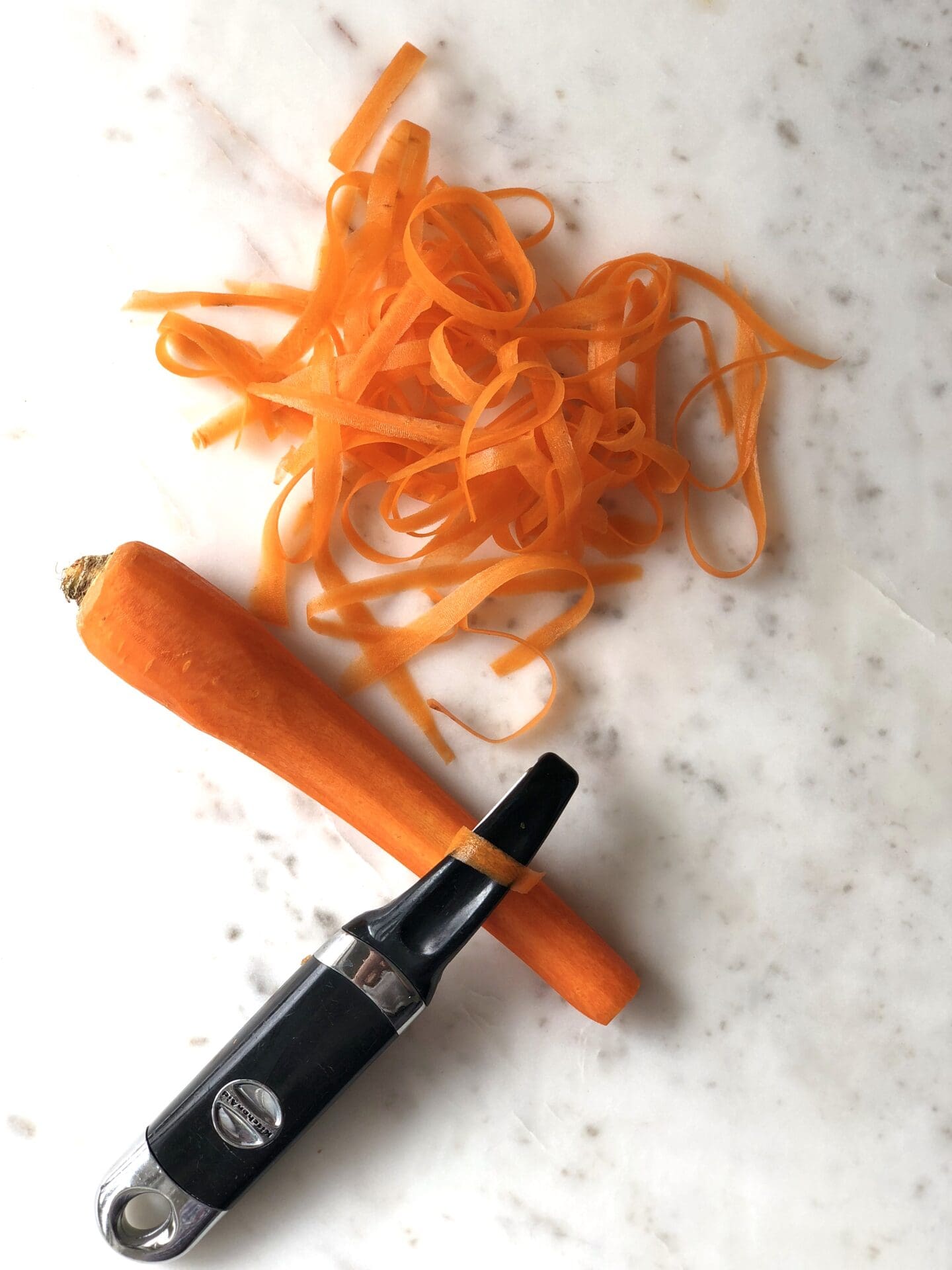 8A5A4F80-449B-41F2-88A5-61A271EFD5B0 Carrot being cut into ribbons with a vegetable peeler