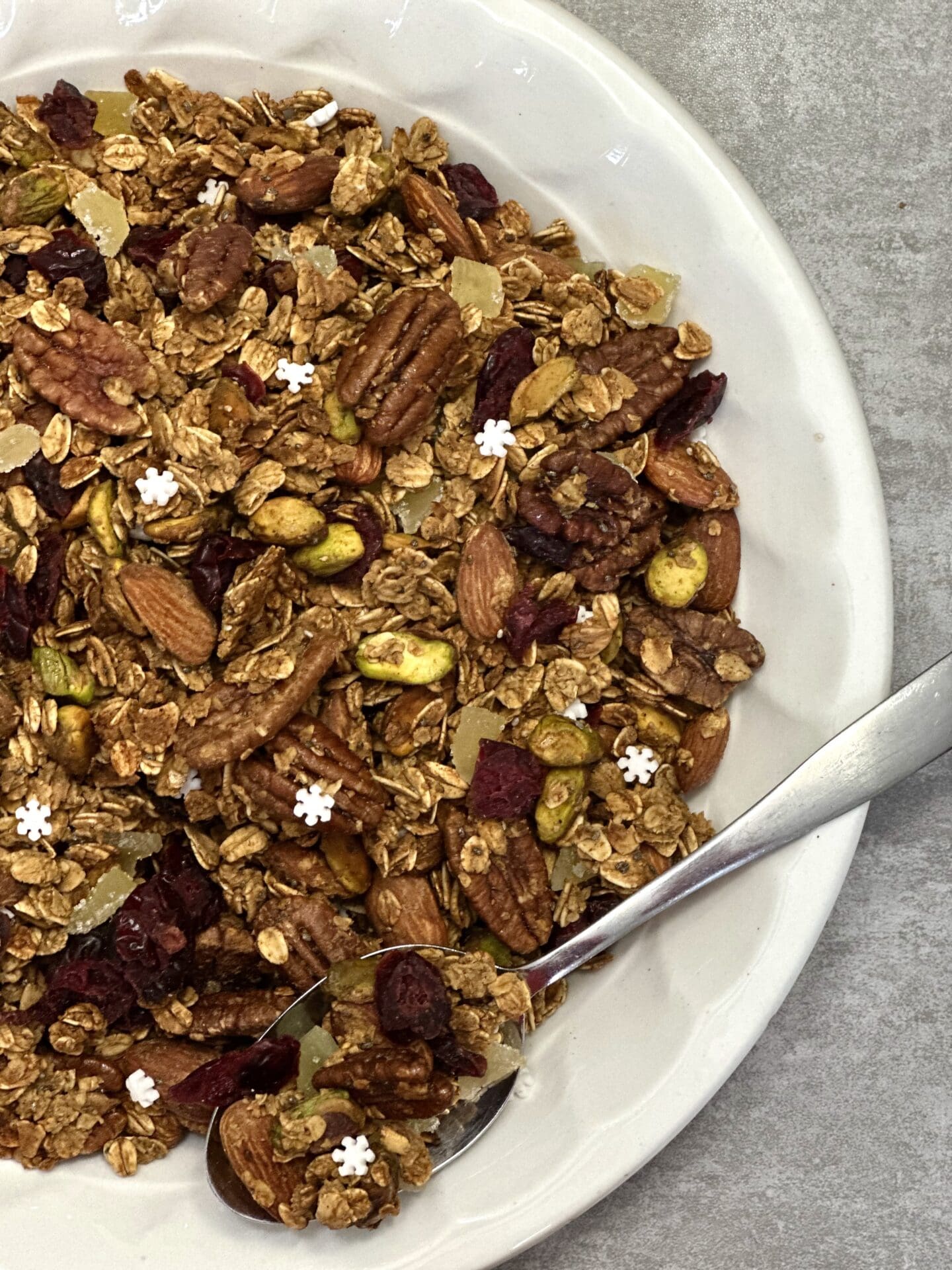 00084988-191E-4A99-AA48-85BC964B1877 Bowl of homemade gingerbread granola with pecans almonds pistachios cranberries pears candied ginger and snowflake sprinkles