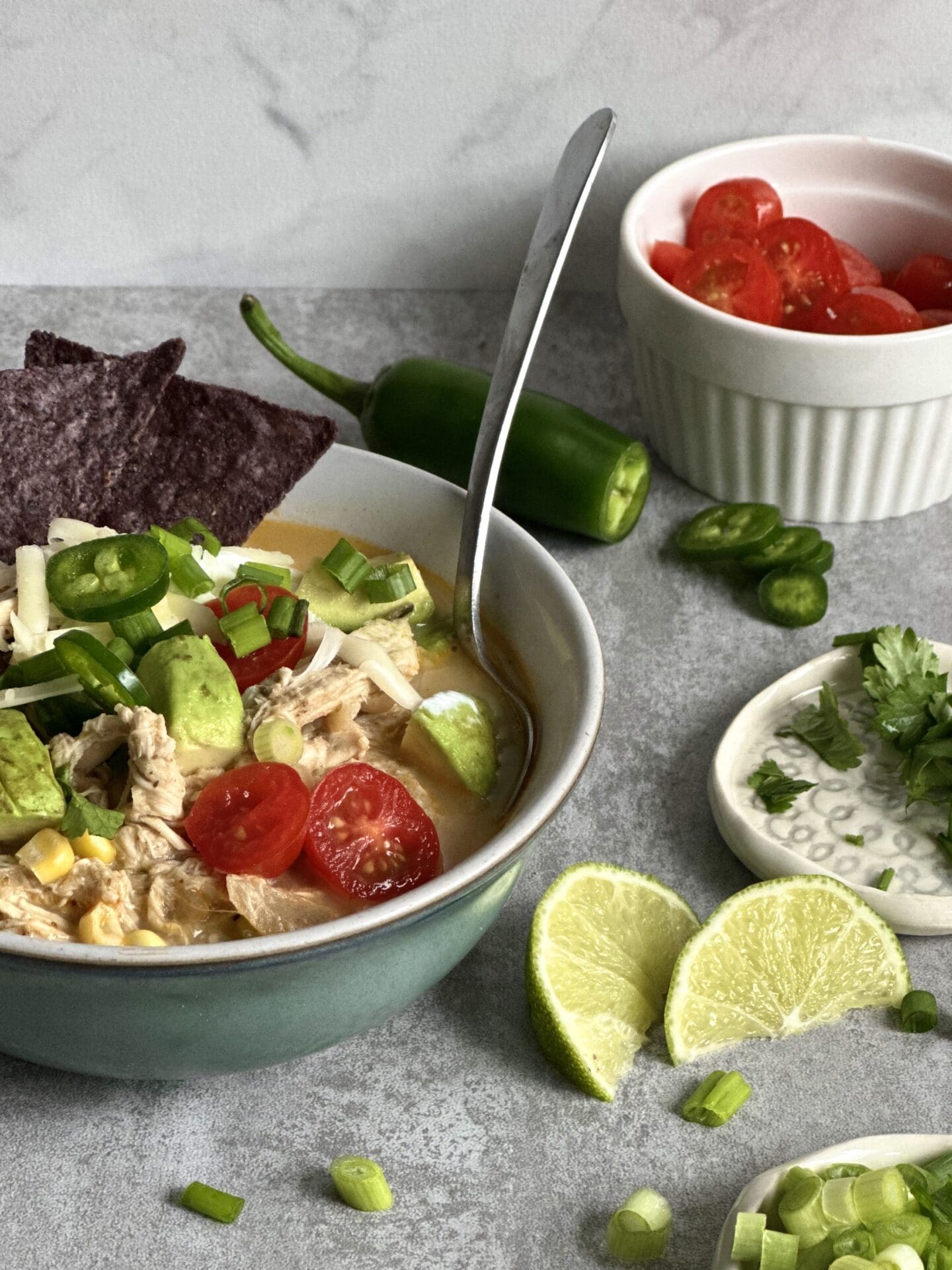 287161F9-FBD2-4F3C-8B51-714B936E56F0 Heaping bowlful of White Chicken Chili surrounded by chopped tomatoes, scallions, blue corn chips, fresh jalapeños and sliced limes