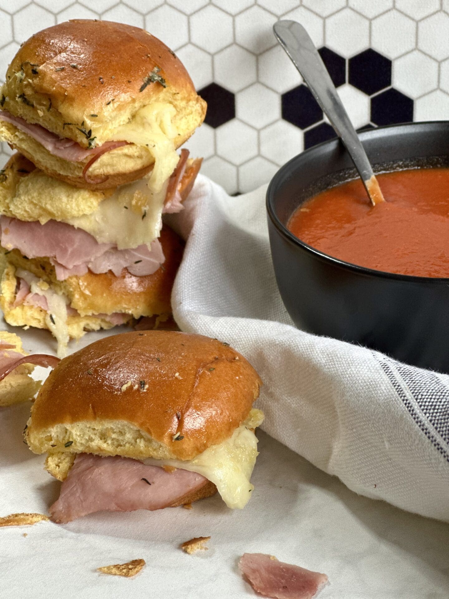 C05B3FD6-F0FE-4B1B-BEC6-353A5EAAA30C Hot and melty ham and cheese sliders stacked up beside a bowl of homemade tomato soup