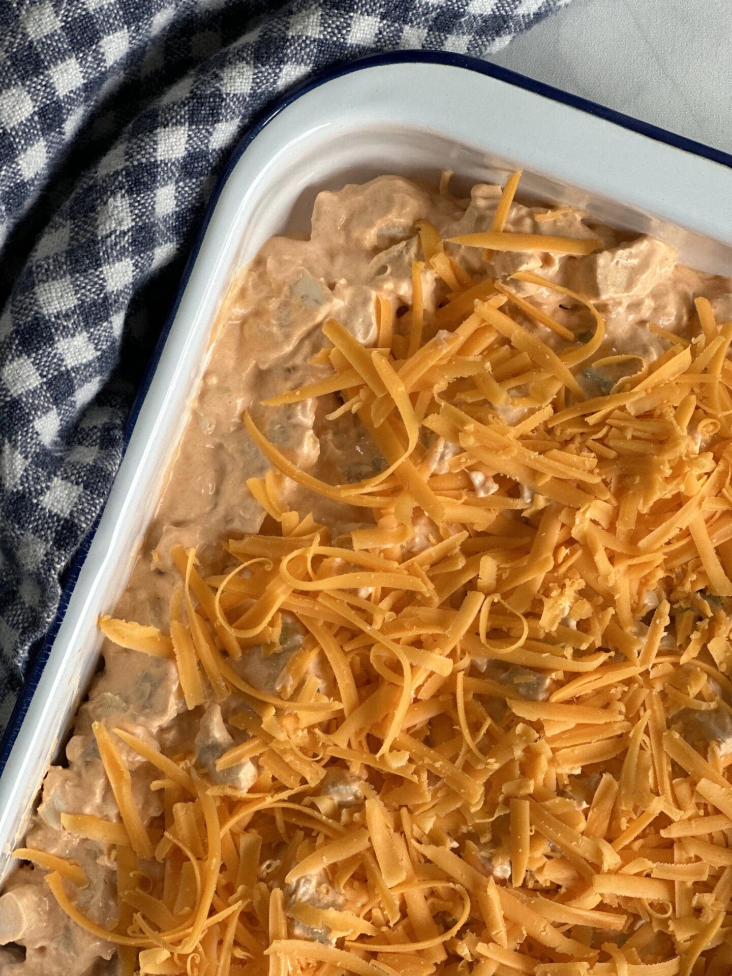 C903039D-9473-40BA-A585-D381B85A6DEE White enamel pan with Hot and Spicy Buffalo Chicken Dip, topped with grated cheddar cheese, ready to be warmed in the oven.