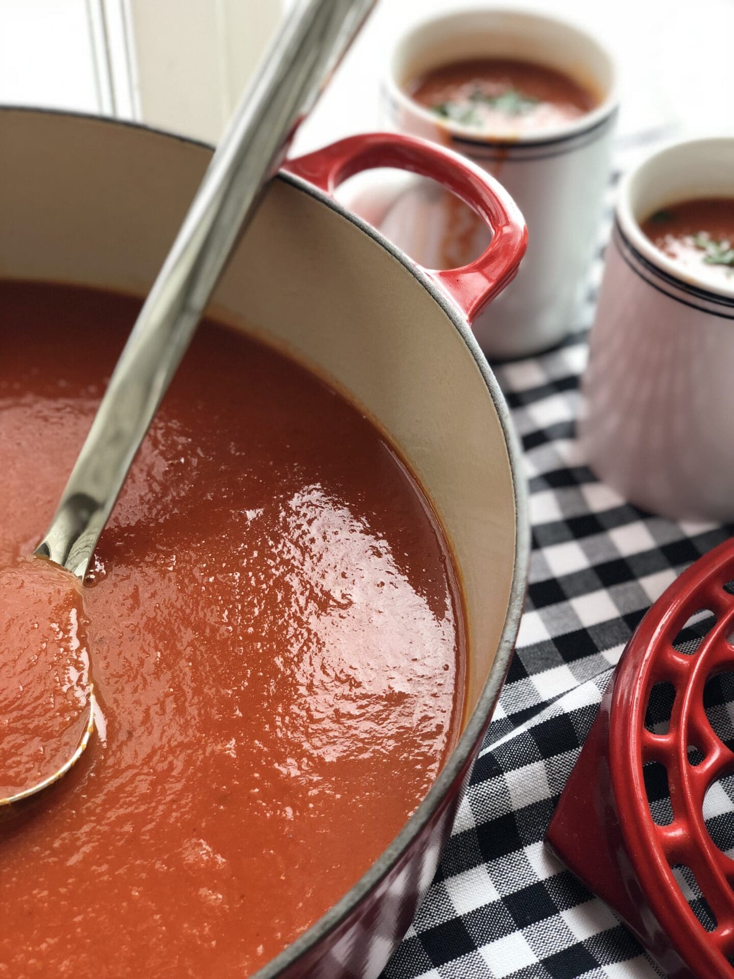 E2D9C80A-4C6D-4DF6-92C9-B26ED5AEF923 A large pot of homemade tomato soup seen from above, with a ladle and mugs for serving