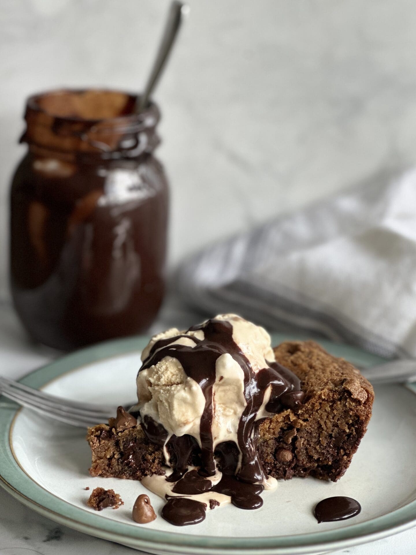 0336E44F-F4B1-4115-A699-FDF65B1951F8 A slice of giant chocolate chip skillet cookie topped with ice cream and hot fudge sauce.