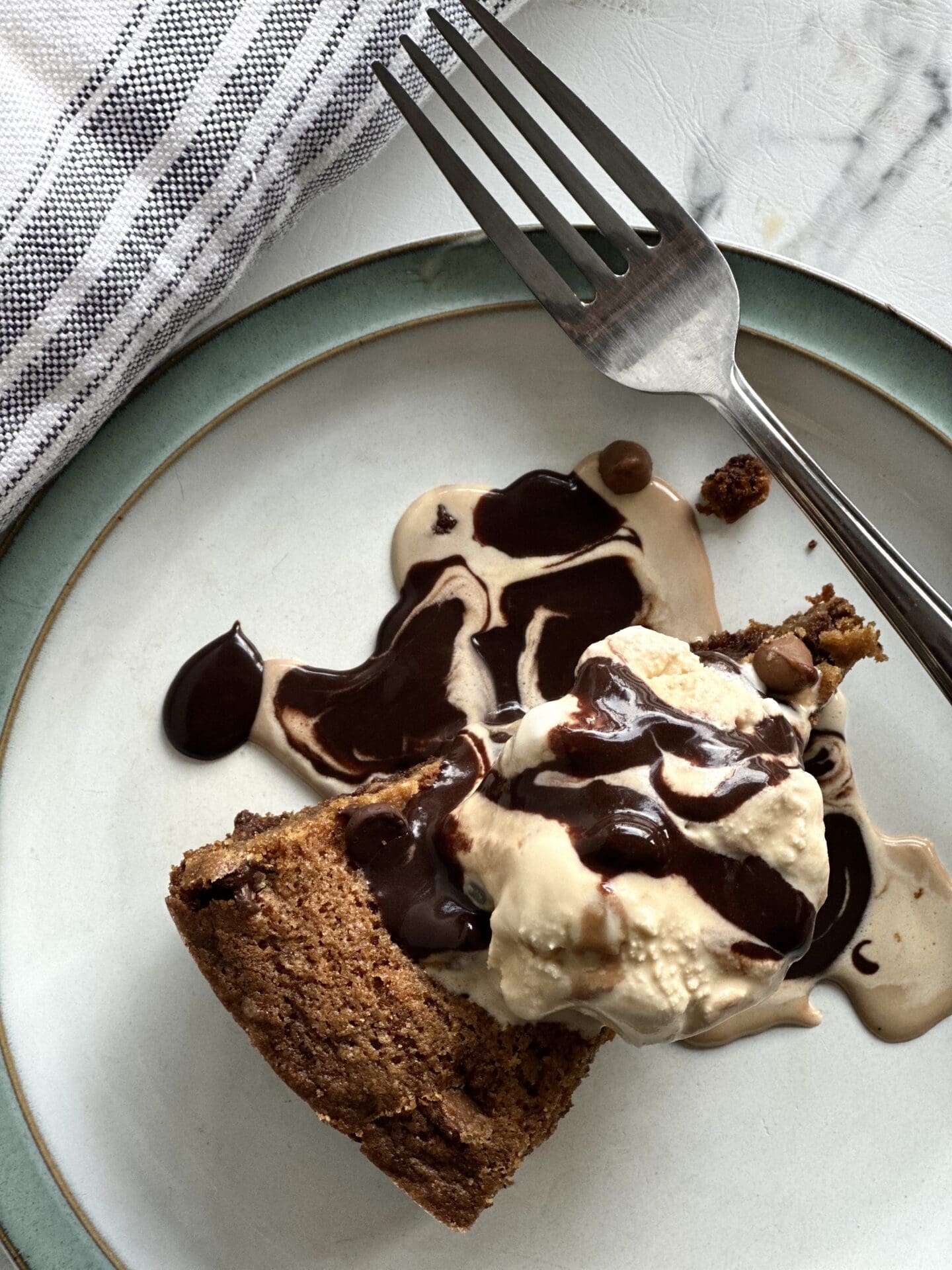 AFCAC82C-BEB3-45AD-8FB4-2FB3224CBF60 A wedge of a giant deep dish chocolate chip cookie seen from above, topped with caramel ice cream and hot fudge sauce