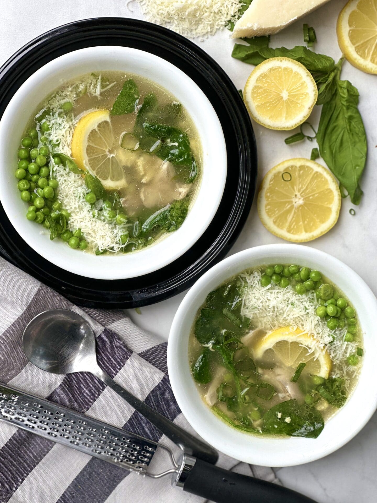 E838880D-0FDB-440F-956D-425D37434654 Two bowls of spring straciatella soup, seen from above garnished with fresh basil lemon peas and freshly grated parmesan cheese