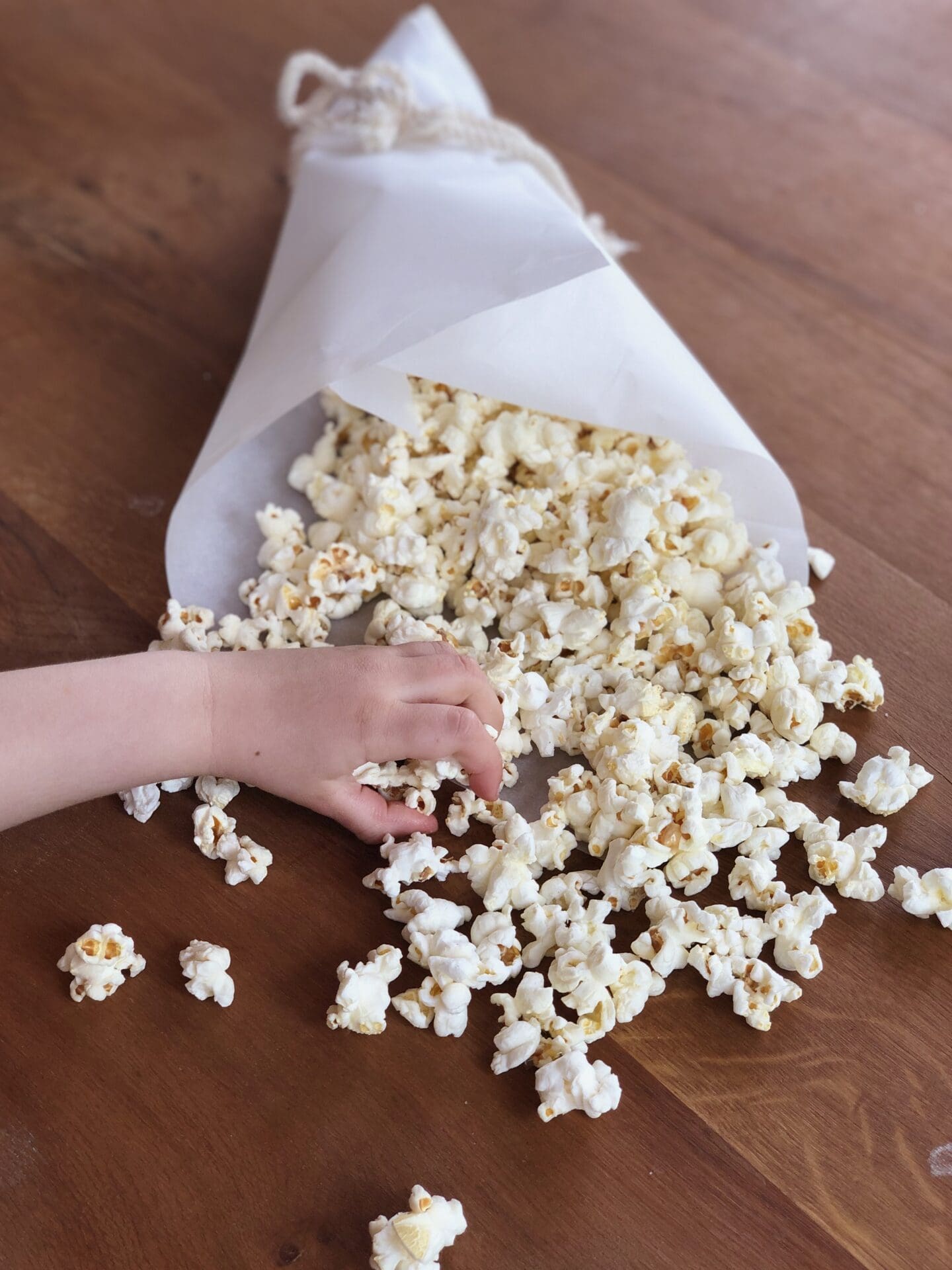 IMG_1609 A little hand reaches into grab a handful of truffle popcorn from a paper cone of popcorn sitting on a wood table