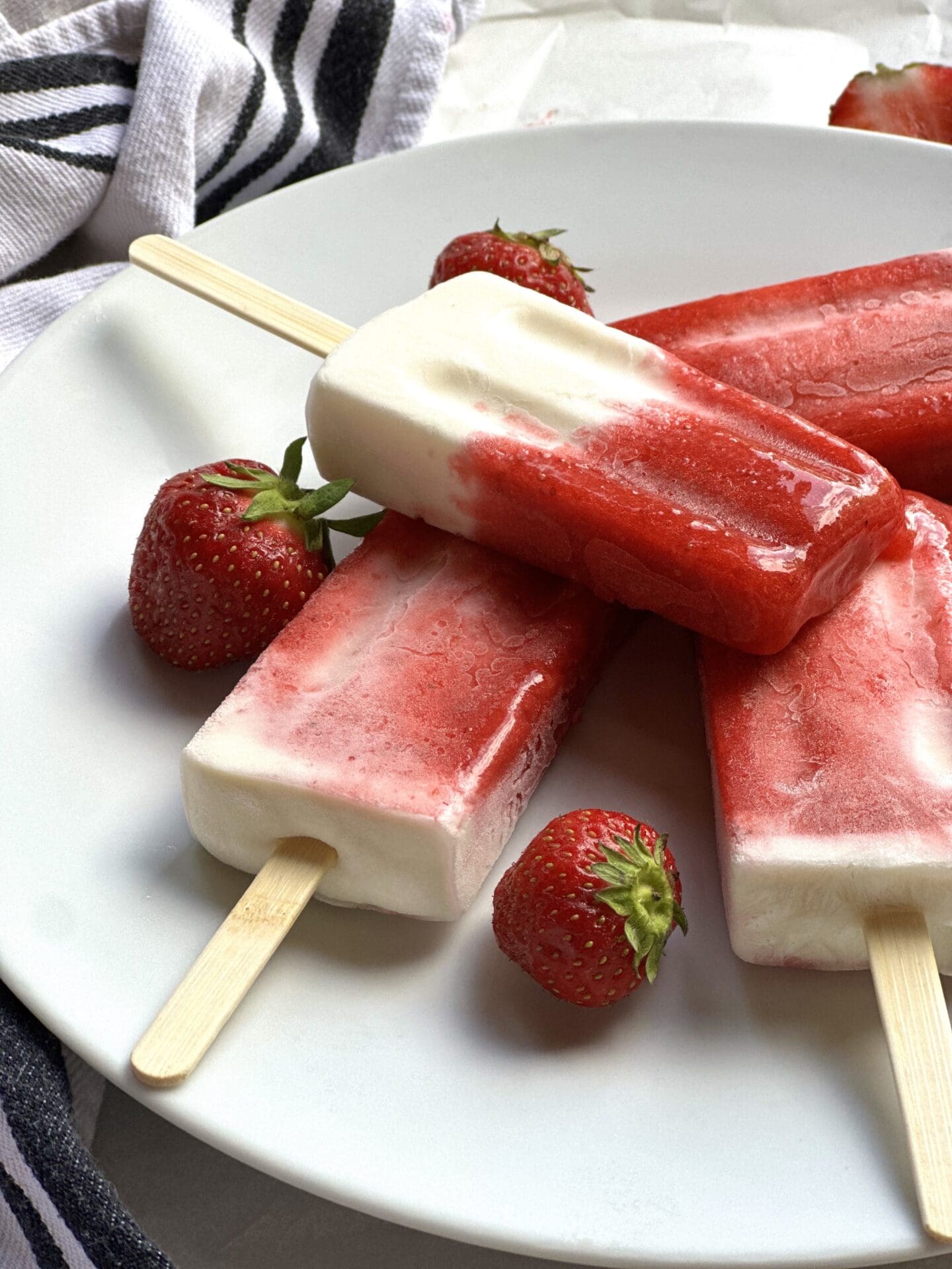 IMG_8680 Plate of strawberries and cream breakfast popsicles seen from the side, surrounded by fresh strawberries