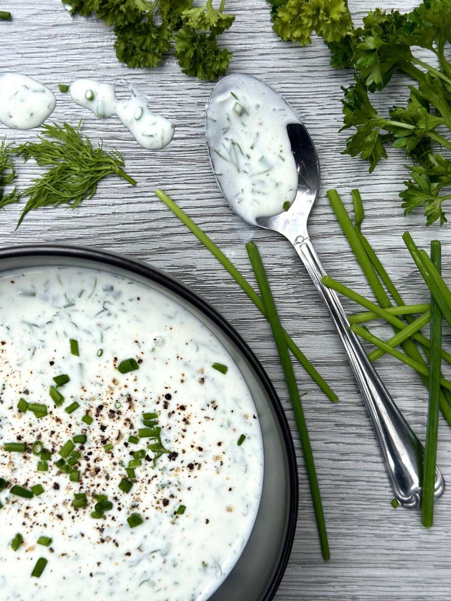 IMG_9340 A bowl of fresh buttermilk ranch dressing on a grey wood board, surrounded by fresh chives, dill and parsley