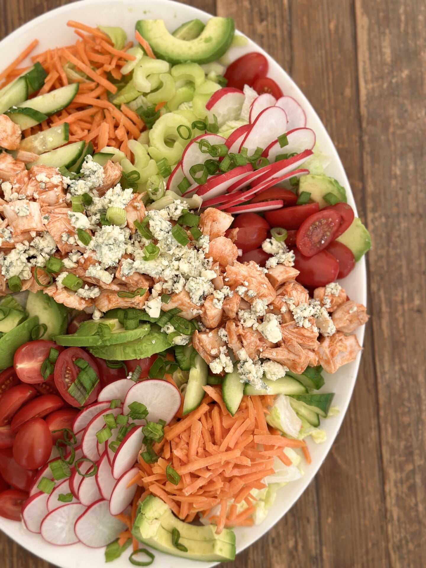 IMG_9342 A large platter of Buffalo Chicken Dinner Salad full of bright fresh vegetables and big chunks of buffalo chicken is seen from above on a wood table