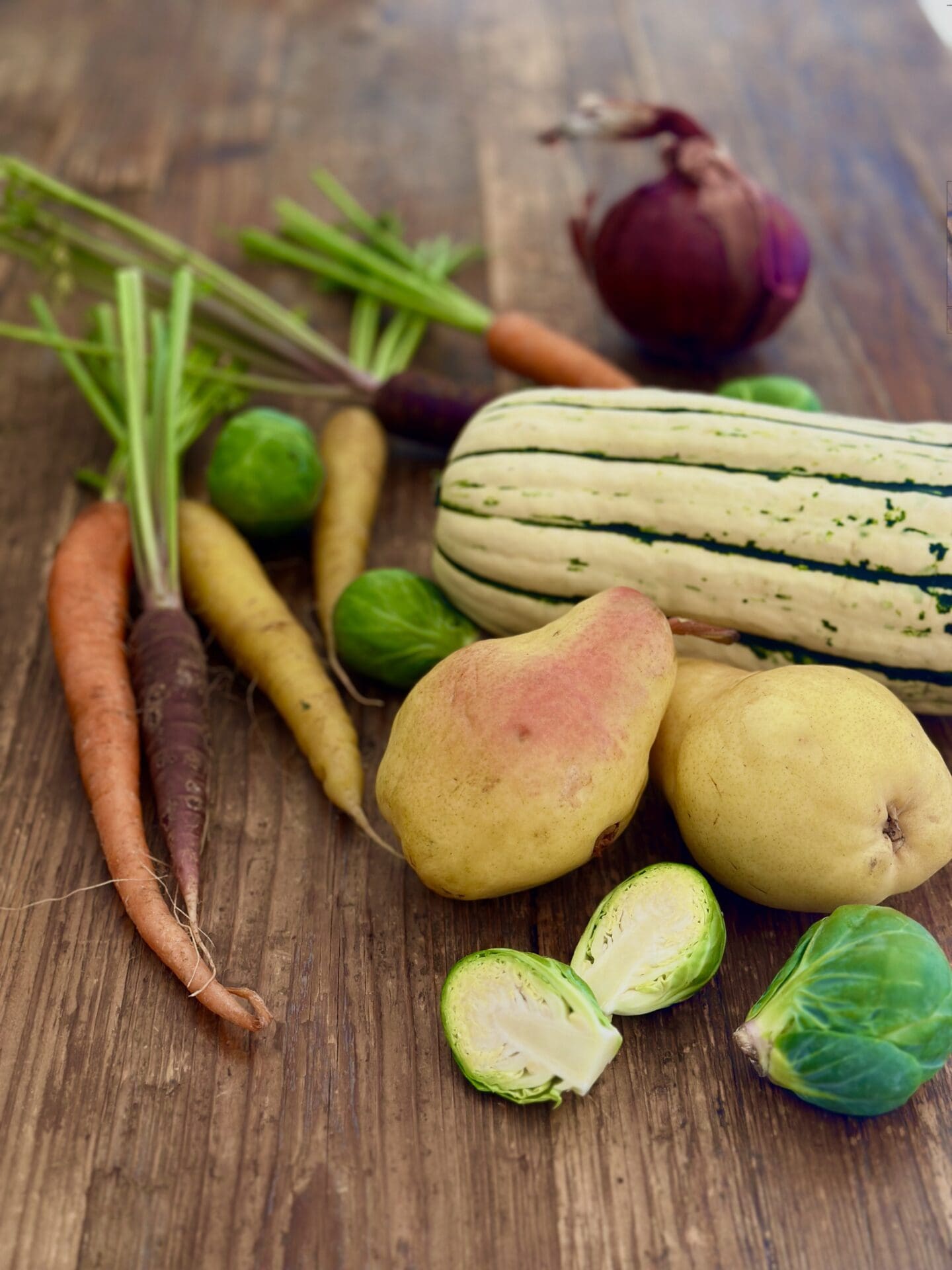 IMG_9423 A selection of colourful carrots, Brussel sprouts, pears, Delicata squash and red onion sits on a wood harvest table ready to be made into a Thanksgiving side dish.