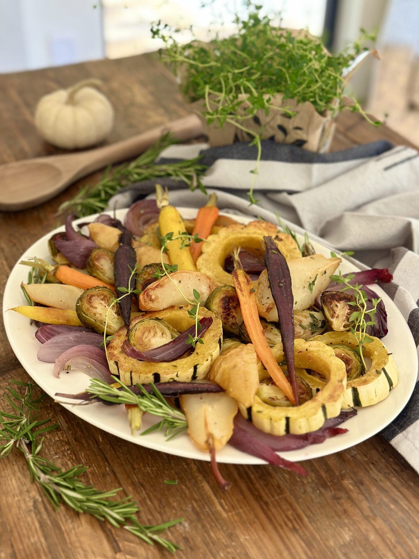 IMG_9447 A Thanksgiving side dish of Maple Butter Roasted Vegetables with Pears sits on a wood table, surrounded by fresh herbs