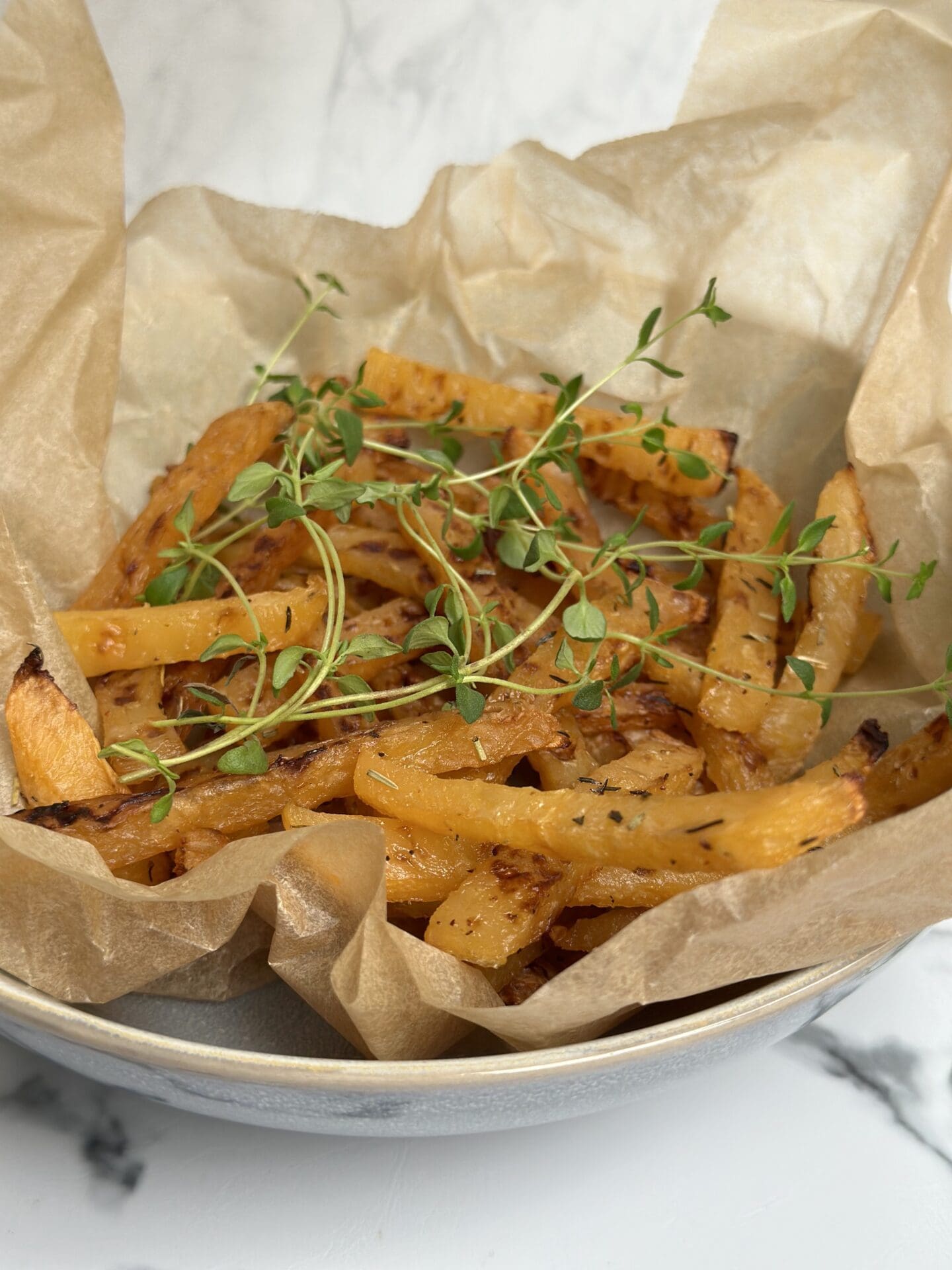 IMG_9704 A brown paper lined bowl of golden oven roasted rutabaga fries sits on a white marble counter top