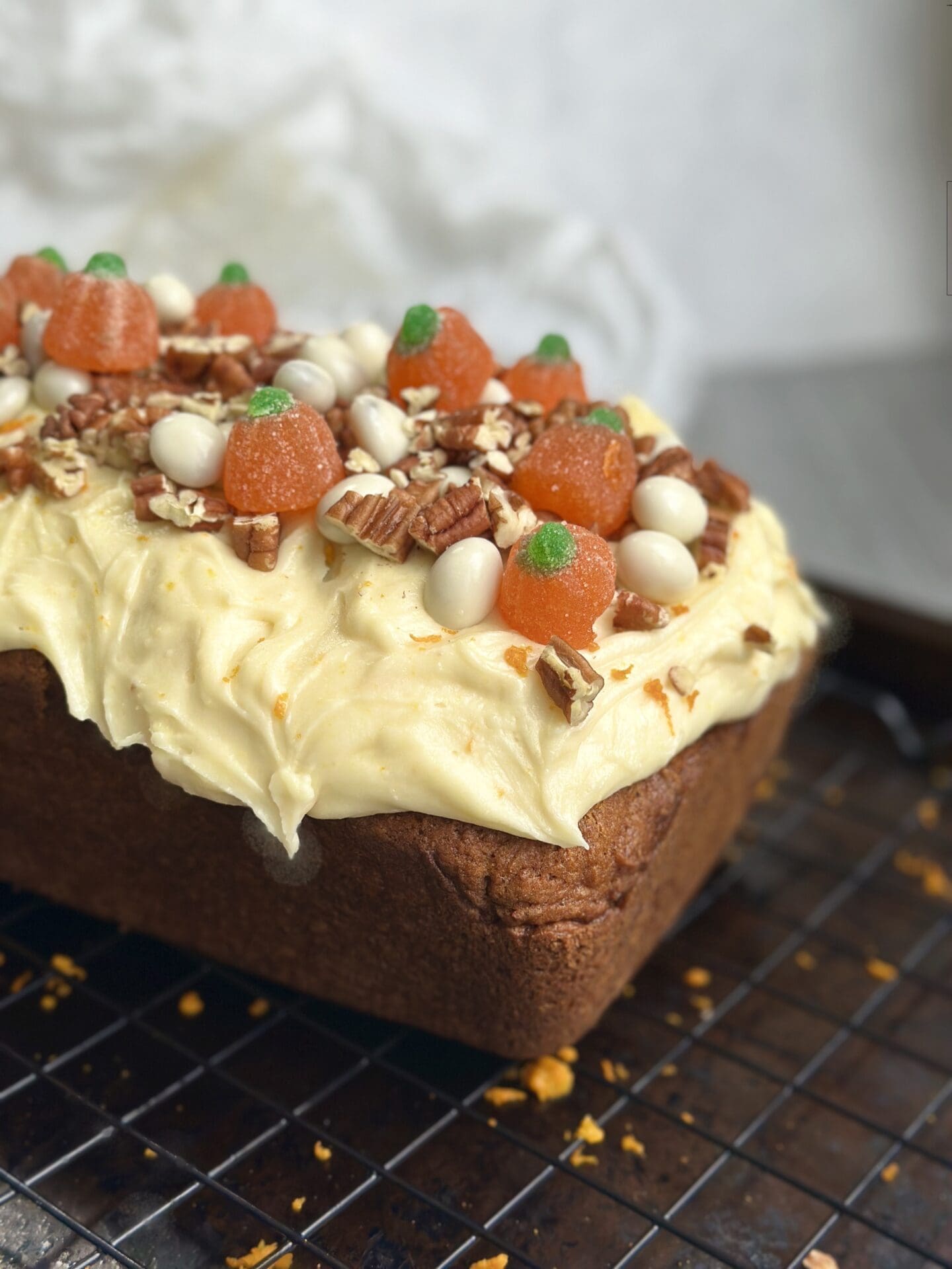 IMG_9739 A loaf of pumpkin bread with orange cream cheese frosting is generously decorated with chopped pecans, yogurt covered raisins and jelly pumpkin candies