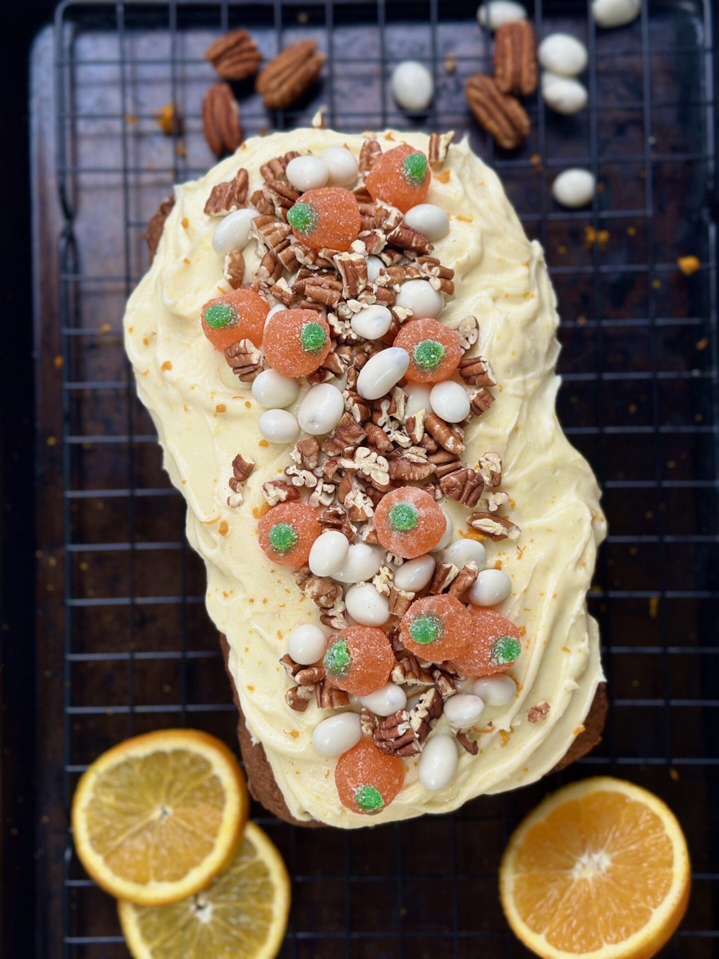 IMG_9742 A decorated loaf with swirls of thick orange cream cheese frosting and loads of candy and pecan toppings is seen from above on a black baking sheet