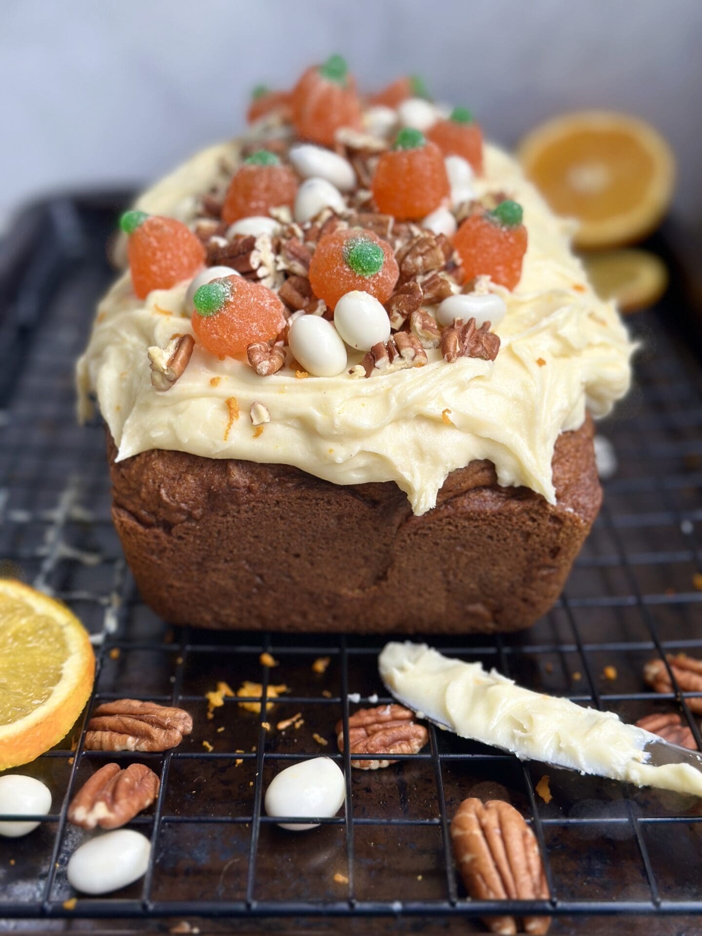 IMG_9753 Pumpkin Bread with Orange Cream Cheese Frosting is seen on a cooling rack, surrounded by the frosting knife, pecans and orange slices