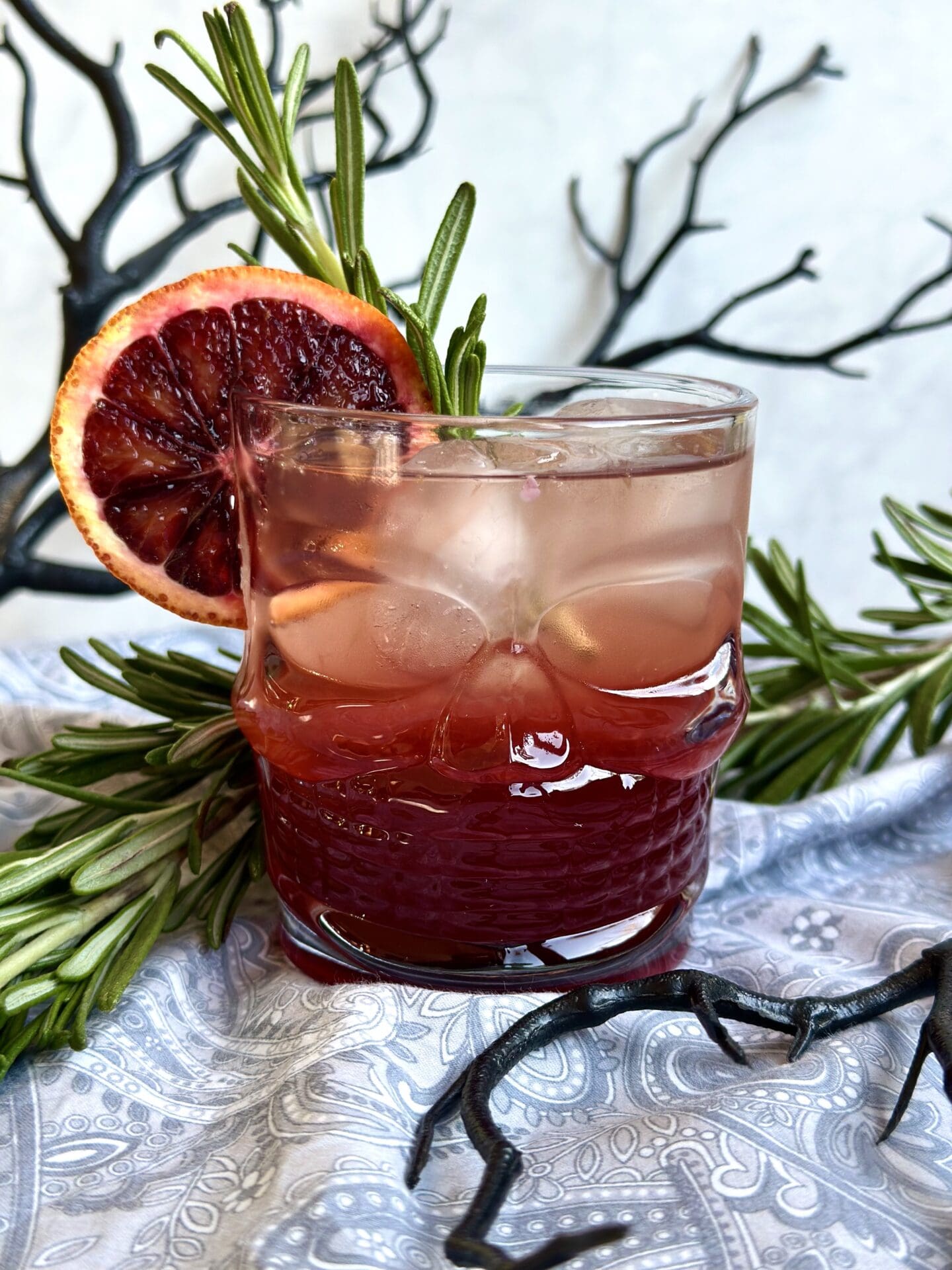 IMG_9837 A blood orange and black currant aperol spritz is served in a halloween themed glass, surrounded by black branches