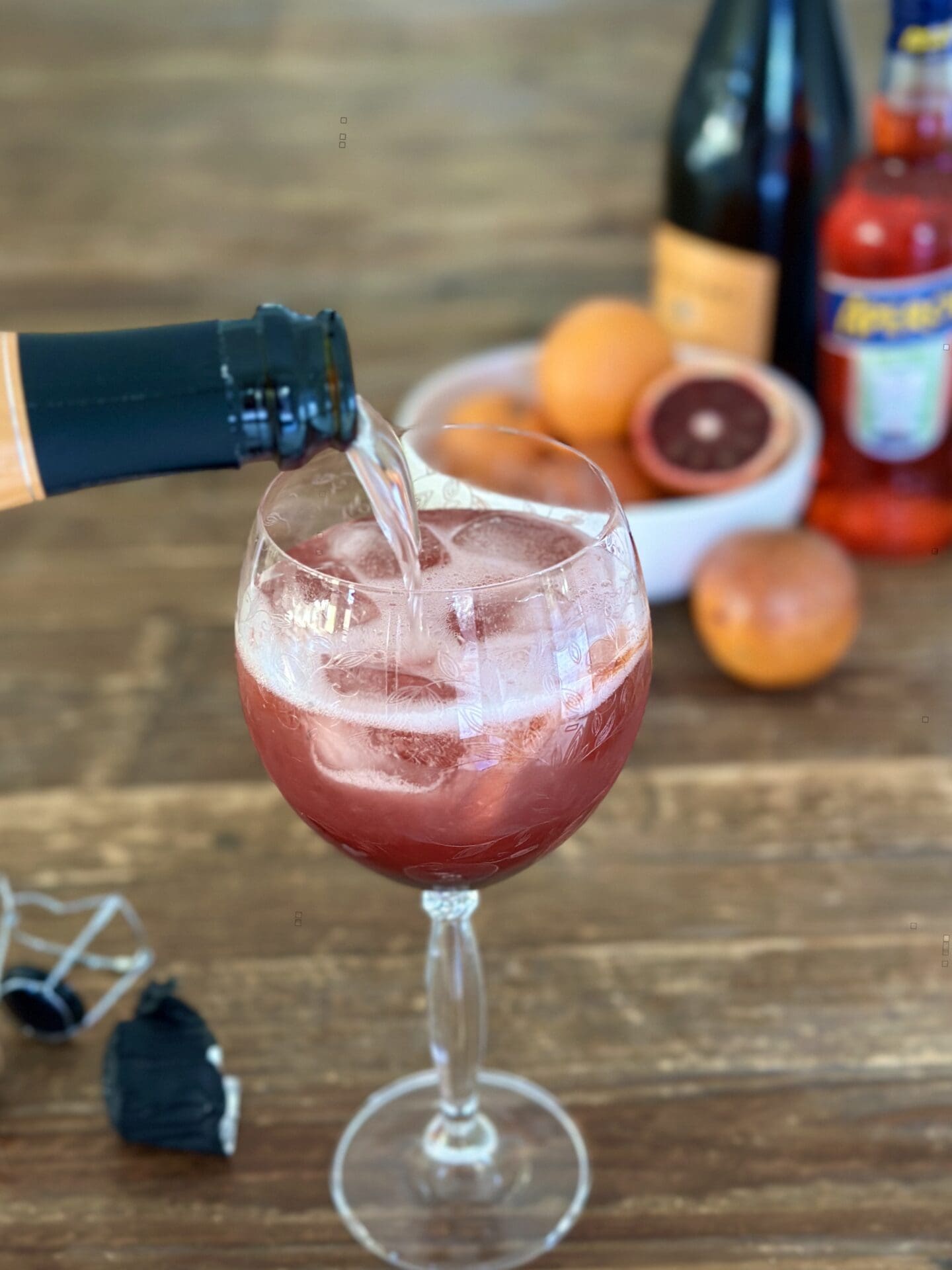 IMG_9854 Prosecco is poured into a blood orange and black currant aperol spritz while it is prepared on a wood table