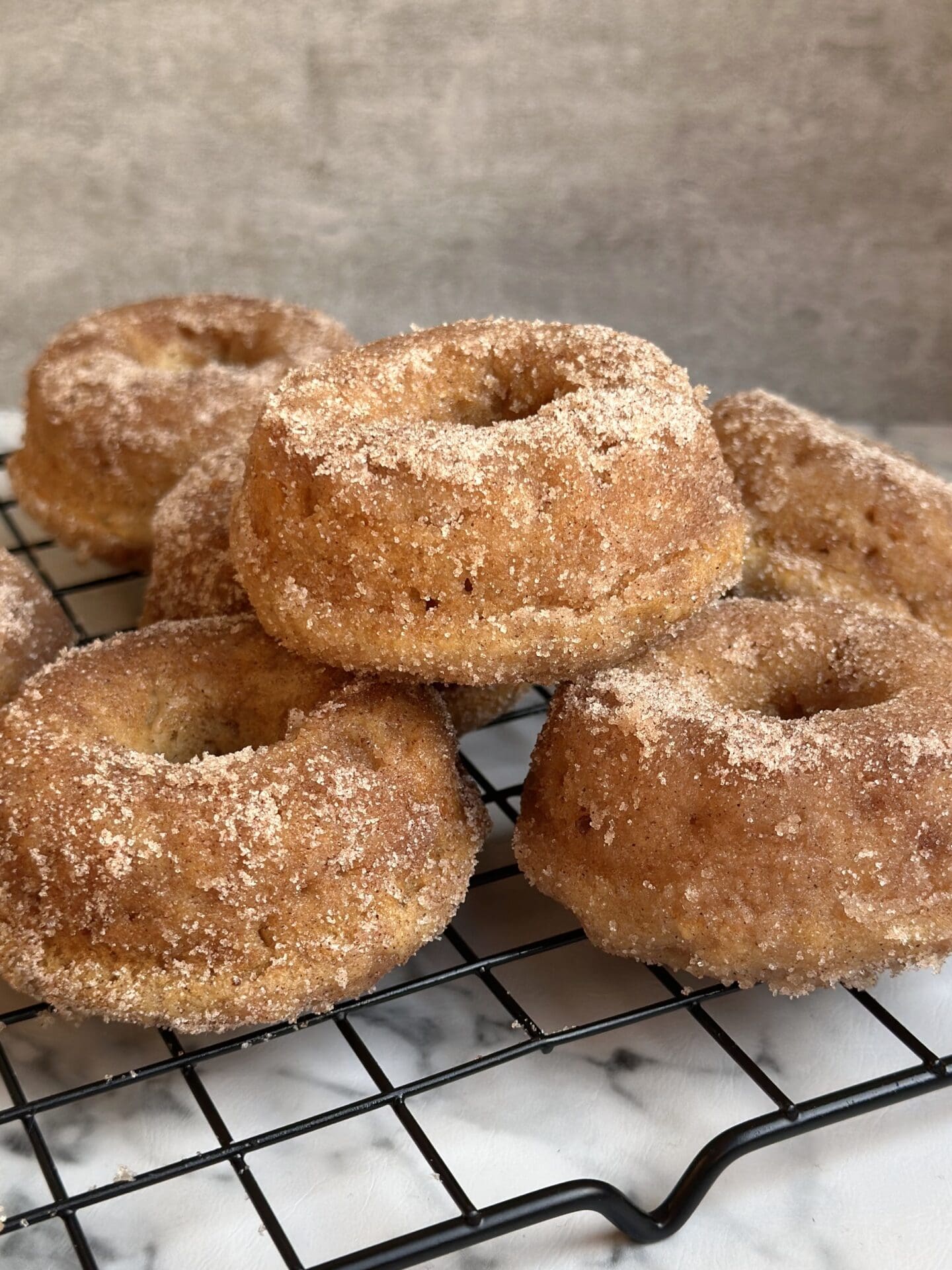 Freshly baked Cinnamon Sugar Donuts are stacked high on a cooling rack