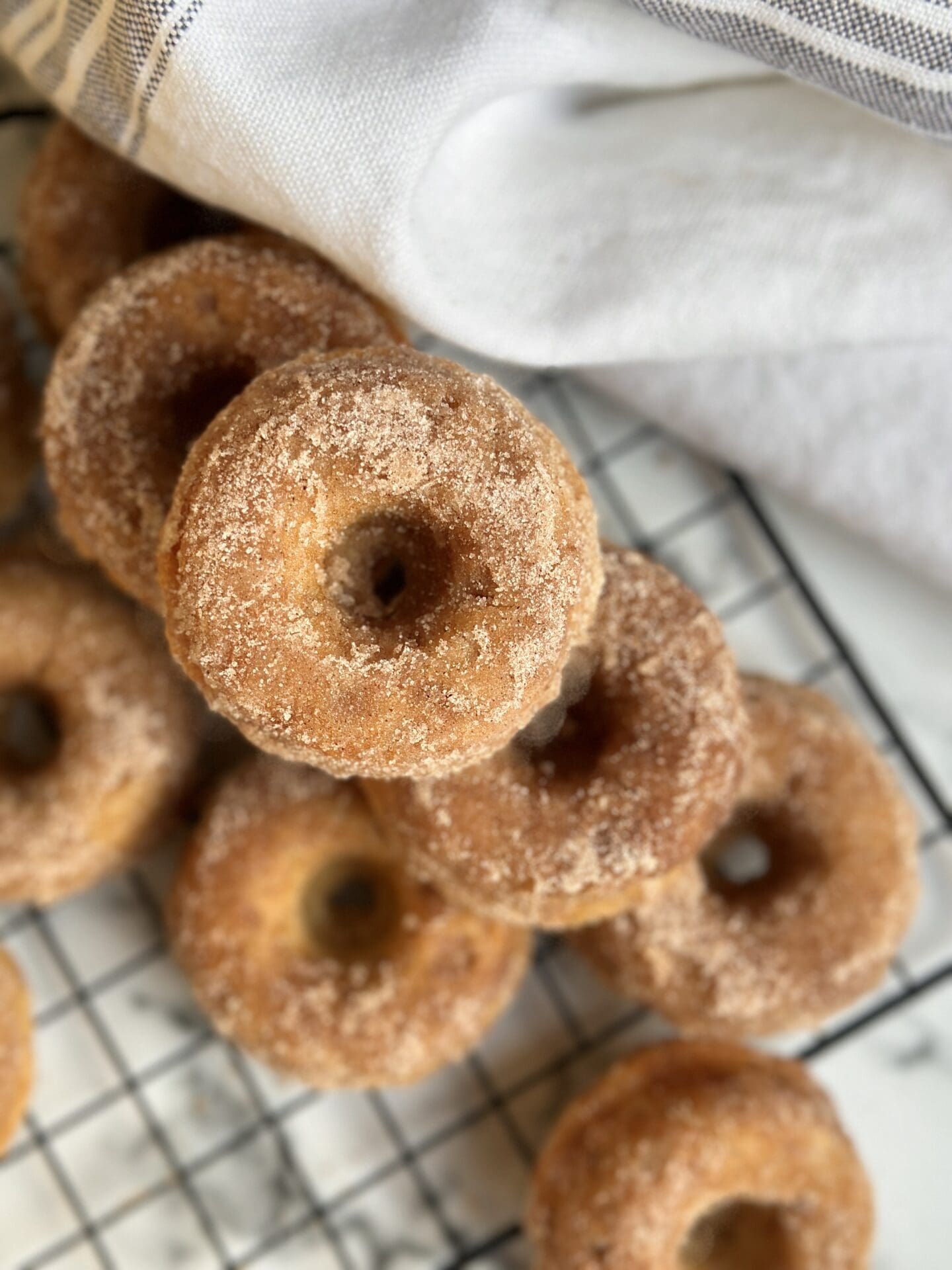 IMG_0036 A stack of freshly baked Cinnamon Sugar donuts on a black wire cooling rack is seen from above