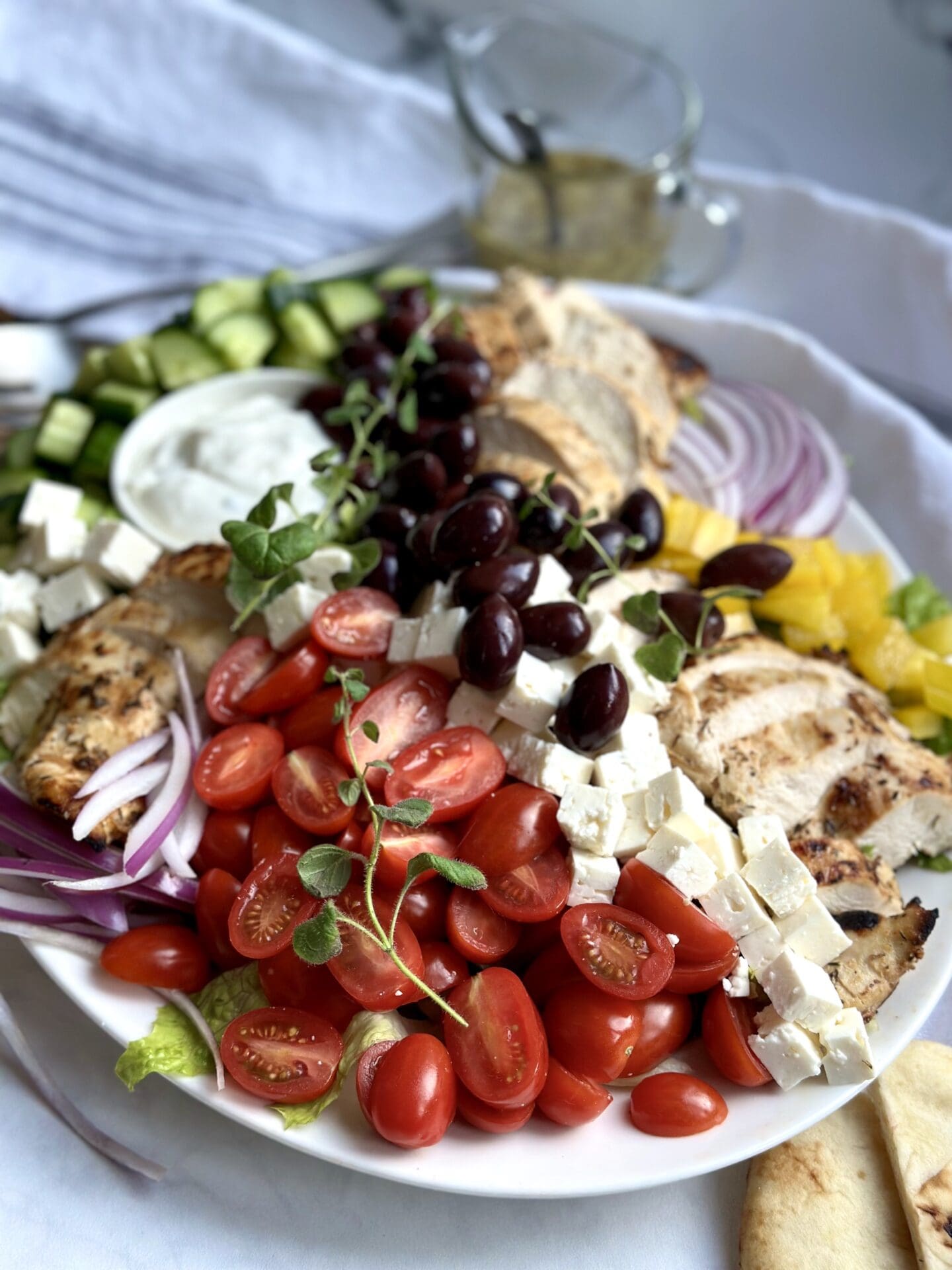 IMG_0448 A large platter of Grilled Chicken Souvlaki Salad is seen from the side, with mounds of fresh colourful vegetables, juicy chicken slices, Kalamata olives and cubes of feta cheese.