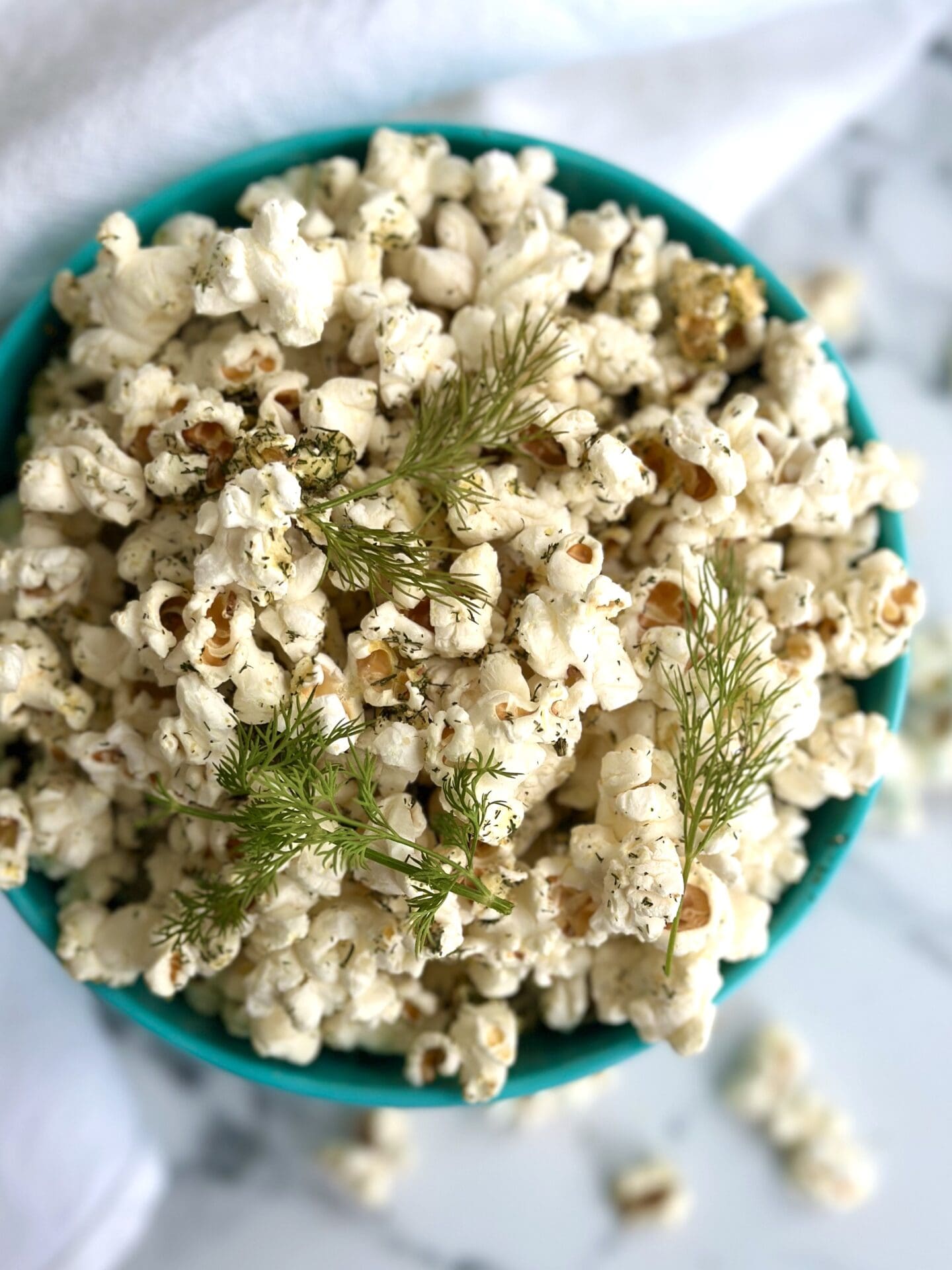 IMG_0958 A bowl of Dill Pickle Popcorn is seen from above garnished with fresh dill sprigs and set on a white marble table