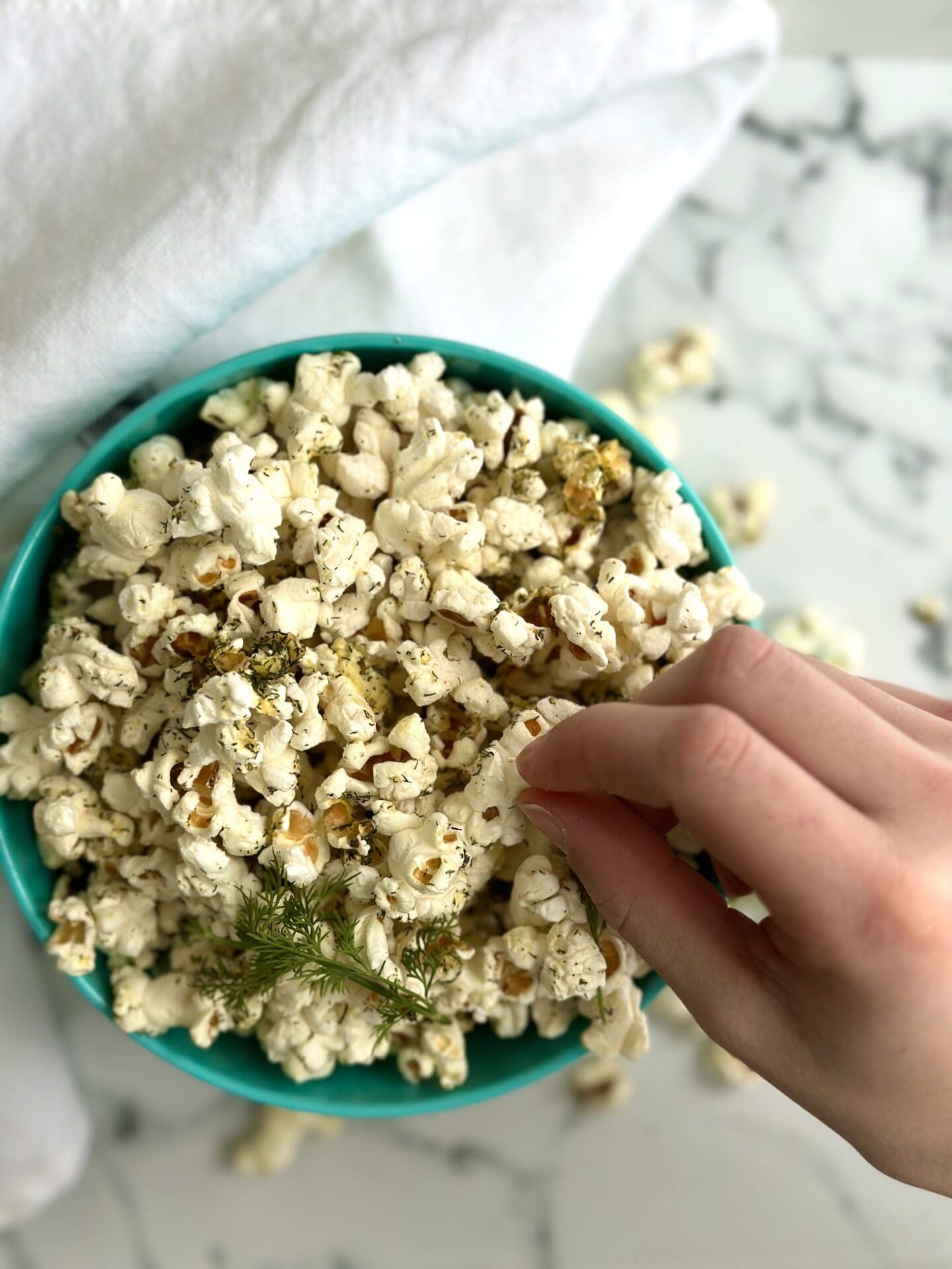 IMG_0965 A bowl of dill pickle popcorn is seen from above with a small hand reaching in to grab a piece