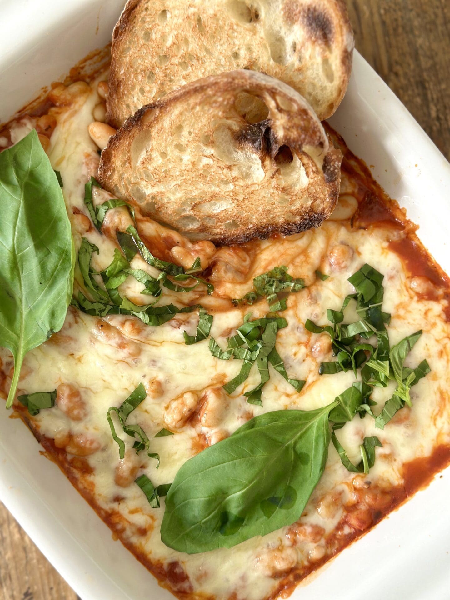 Easy Cheesy Beans with Garlic Toast A pan of Easy Cheesy Beans is seen from above garnished with fresh basil and slices of garlic bread