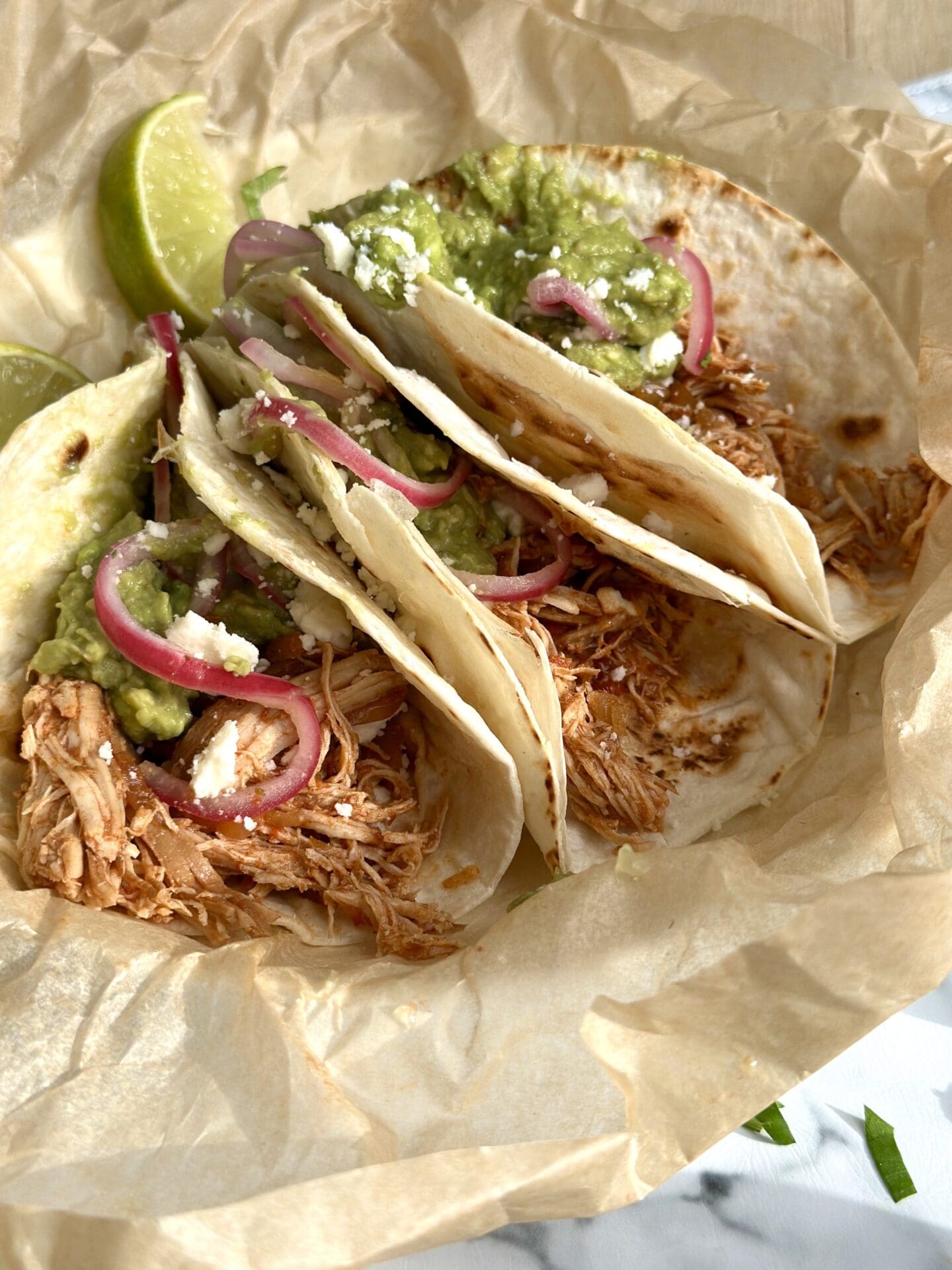 IMG_1246 A trio of pulled chicken tacos are topped with guacamole and pickled red onions
