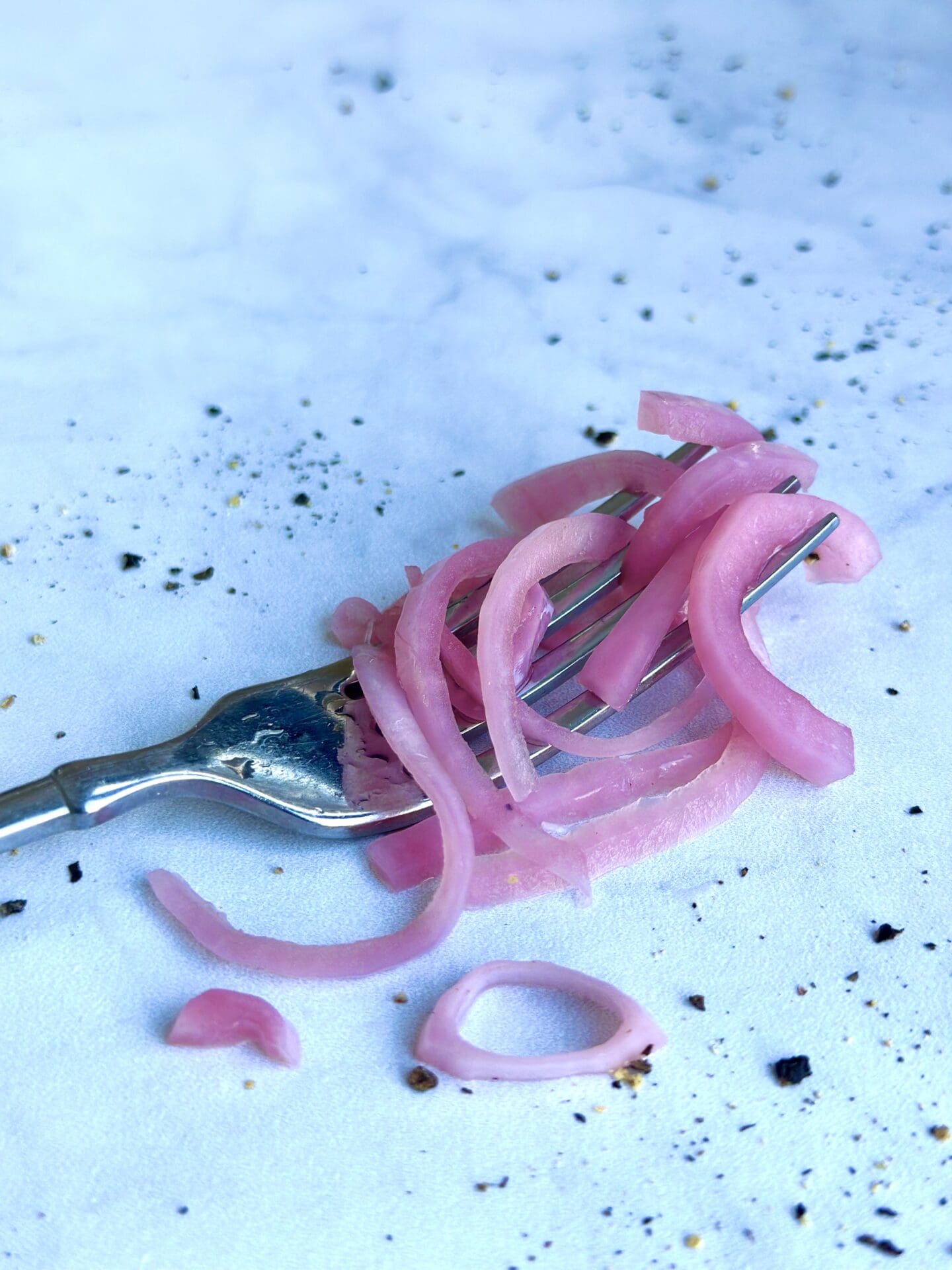 IMG_1272 A forkful of tangled bright pink pickled red onions sits on a white marble table