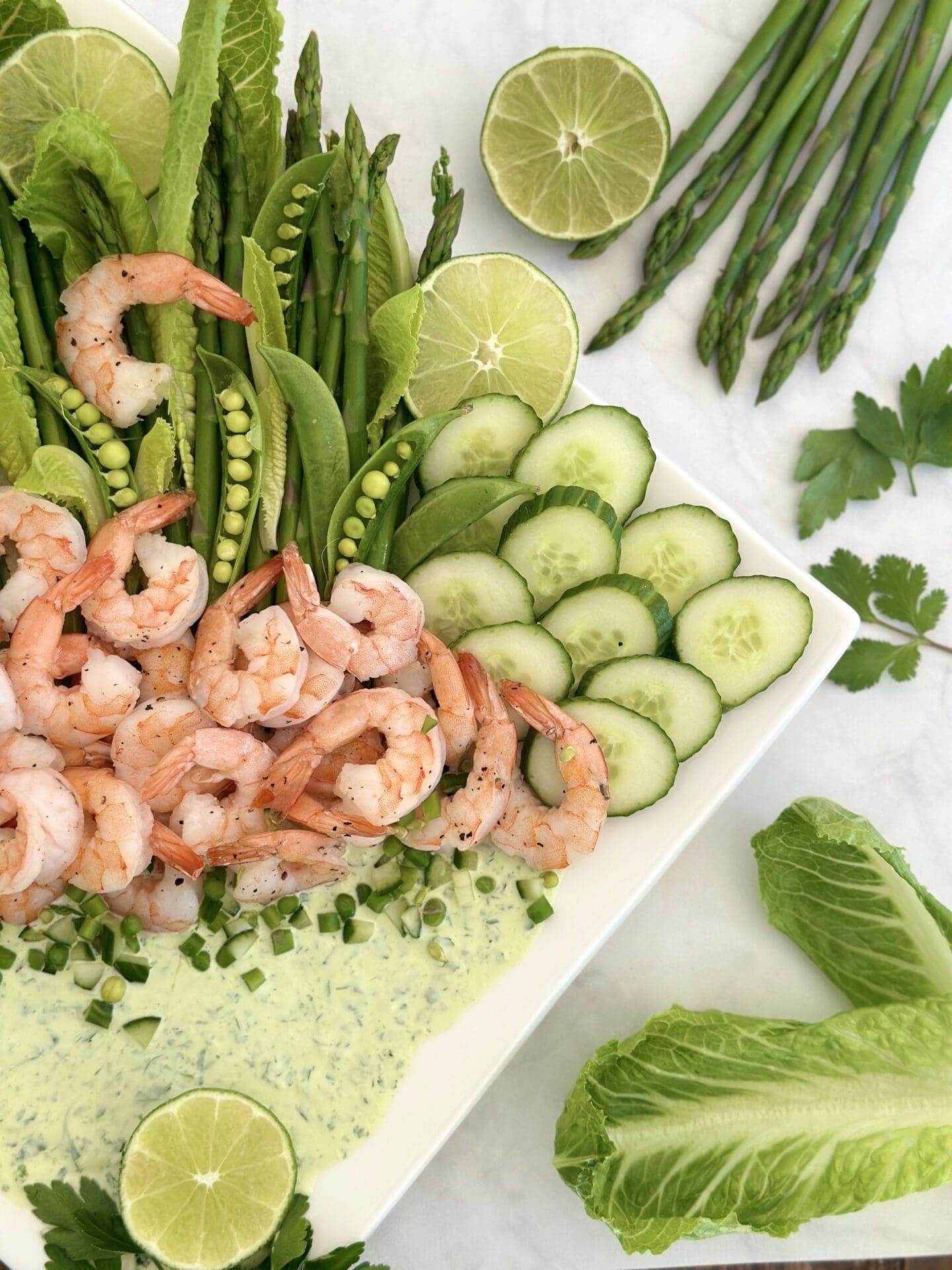 IMG_1440 Half of a platter of shrimp with spring vegetables and a creamy herb dip is seen from above surrounded by fresh herb springs and fresh veggies
