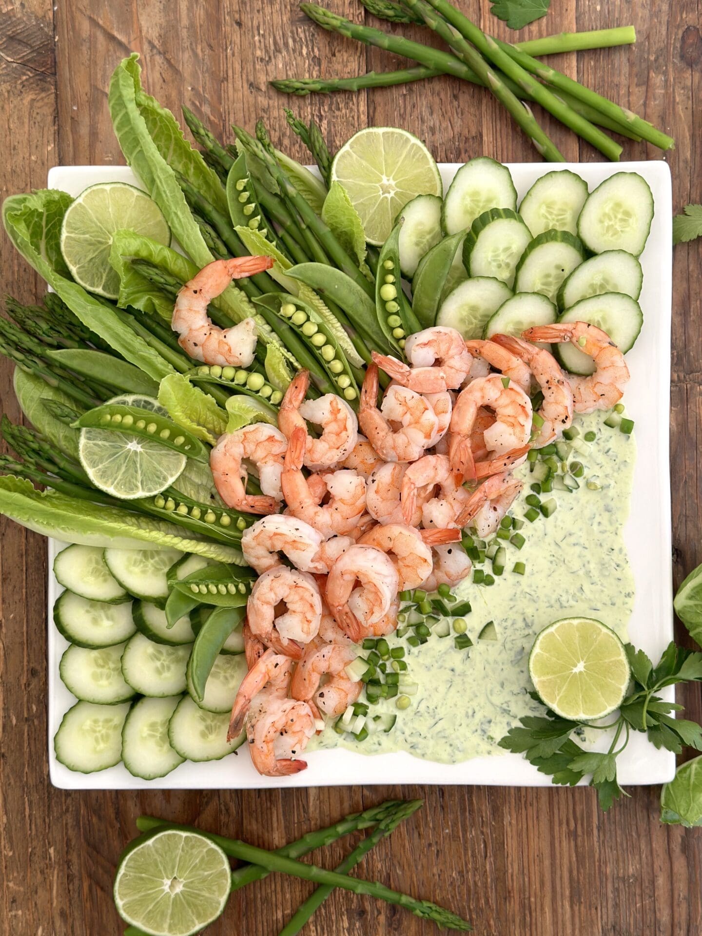 IMG_1449 A beautiful platter of roasted shrimp with asparagus, cucumber, snap peas and romain is seen from above garnished with fresh herbs and lime slices
