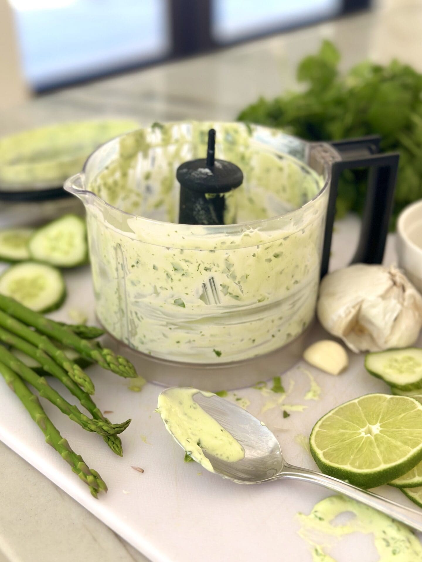IMG_1477 The bowl of a food processor is seen filled with creamy herb dip and surrounded by asparagus, lime, cucumber and fresh herbs