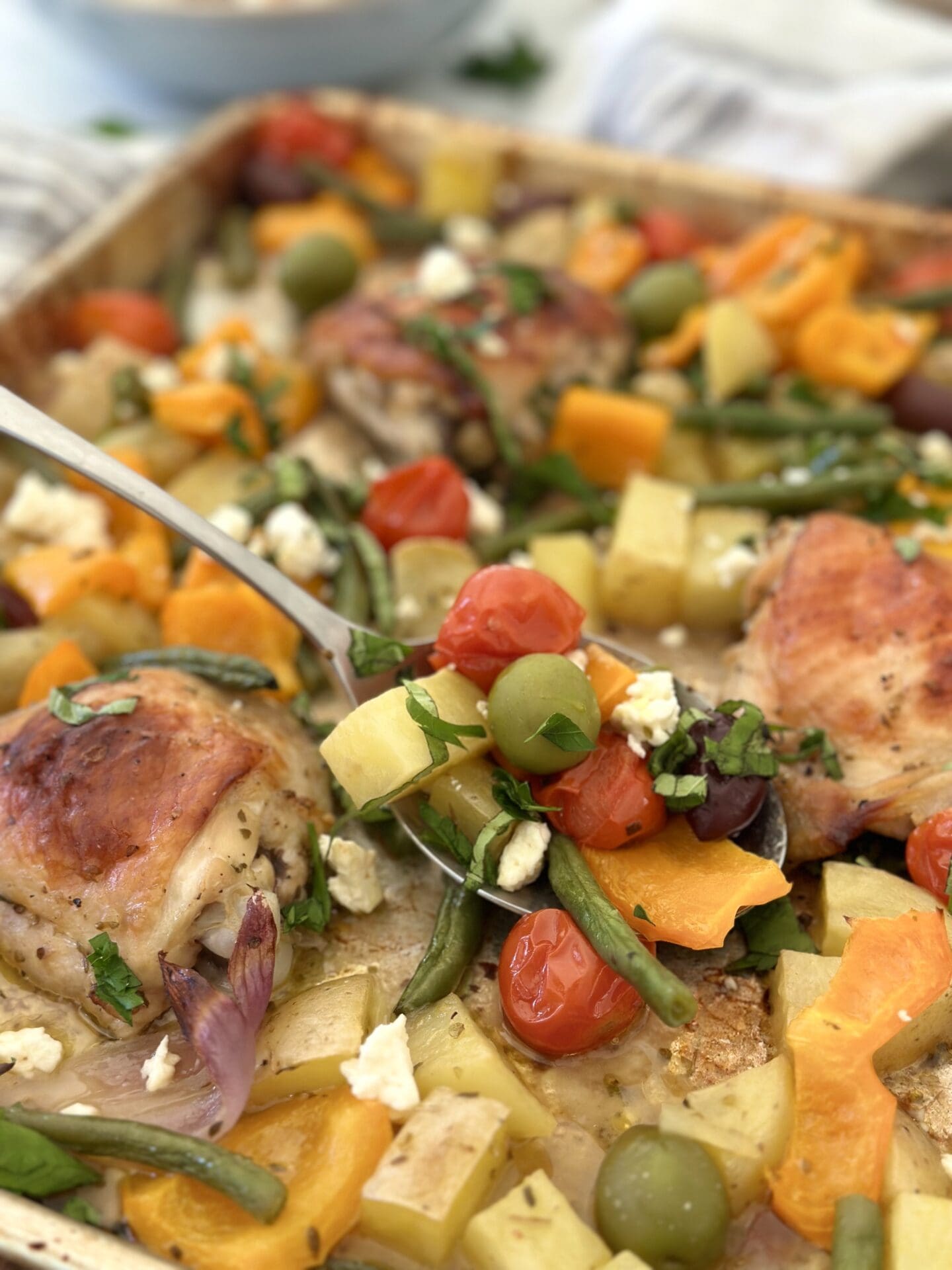 IMG_1719 A large spoon scoops roasted vegetables, olives, fresh herbs and feta cheese from a large tray of Greek Chicken Sheet Pan Dinner