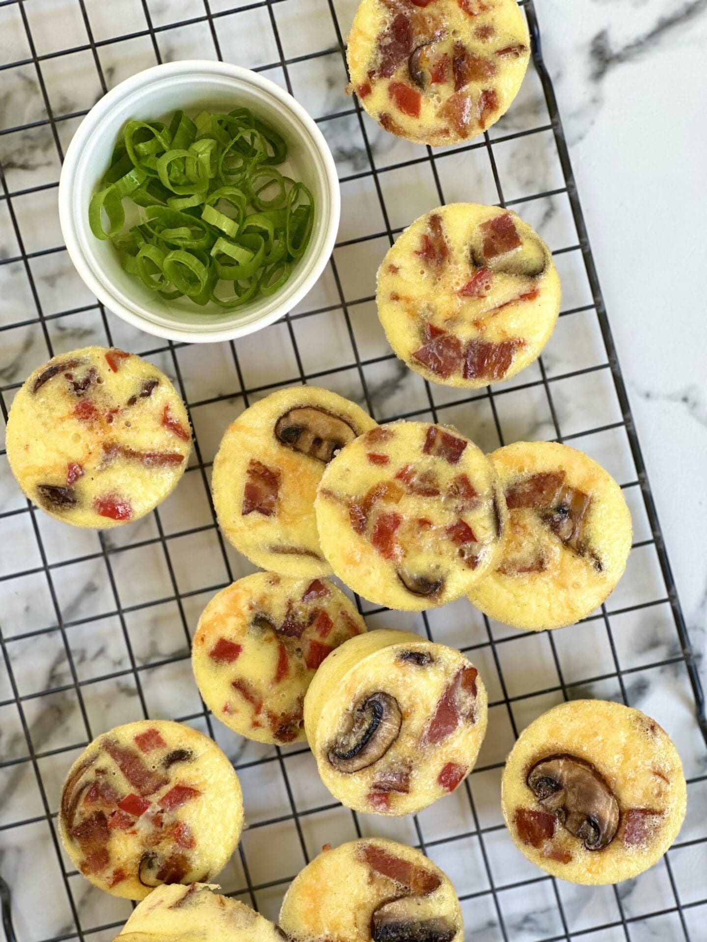 IMG_1840 A batch of oven baked egg bites with bacon, mushroom and peppers is seen from above, cooling on a black wire rack