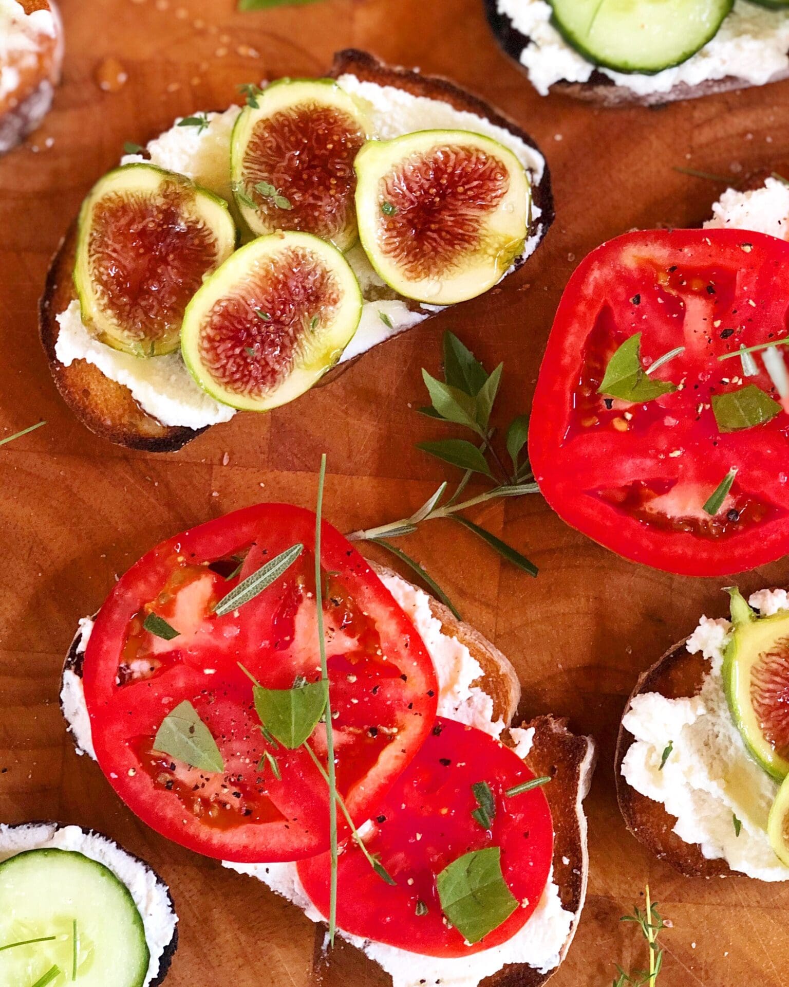 36961AFB-DCD1-4F39-8CBE-3650E977DAA8 Open faced sandwiches are seen from above, slathered with homemade ricotta cheese and some topped with fresh tomatoes and herbs, and some topped with fresh fig slices and honey.