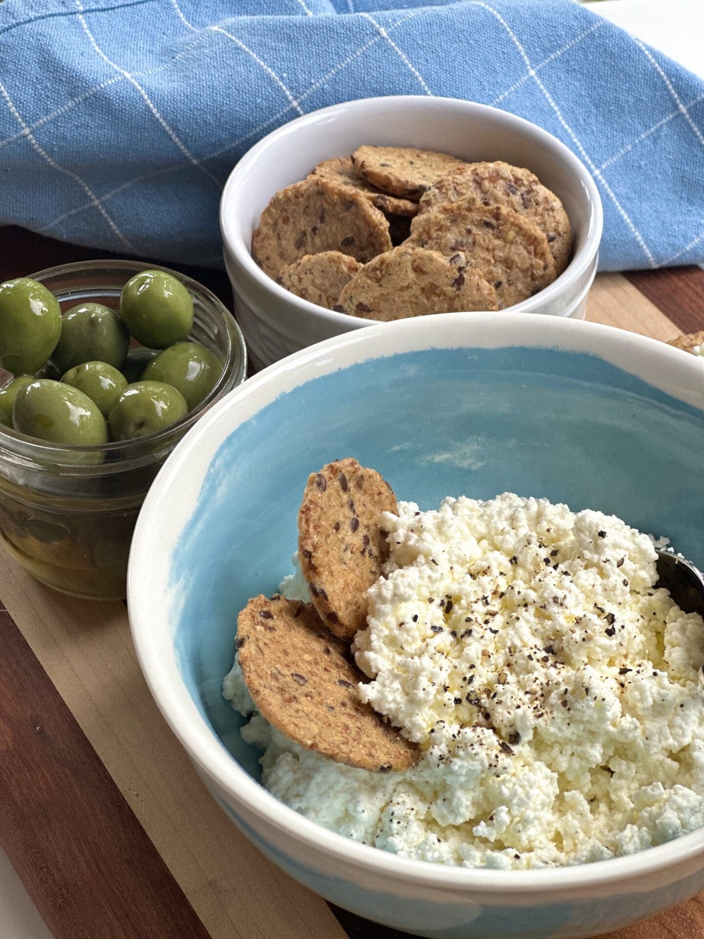Homemade ricotta cheese served with crackers and olives A bowl of homemade ricotta cheese is seen on a serving board with crackers and olives