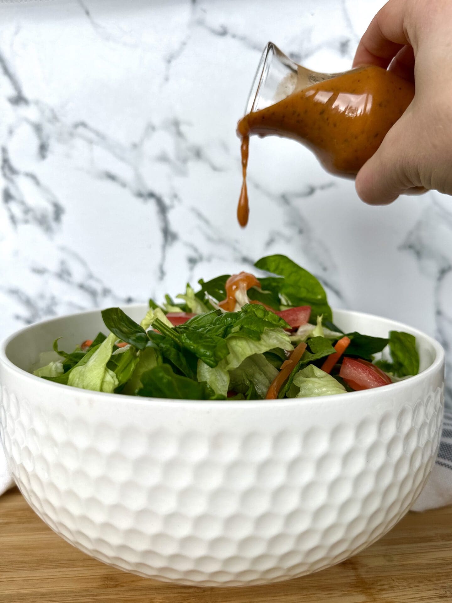 IMG_3514 A hand pours Sundried Tomato Vinaigrette over a big white bowl filled with a green salad