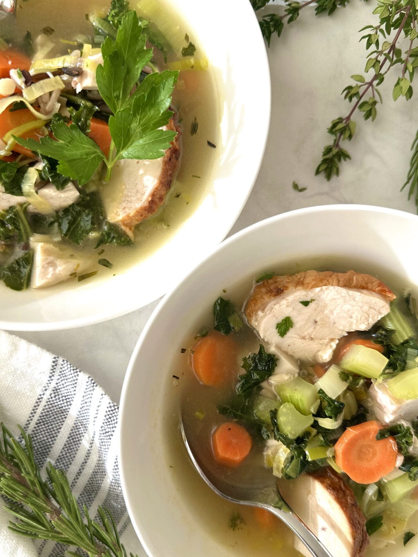 IMG_3715 Two individual bowls of turkey, leek and wild rice soup sit on a white marble table surrounded by fresh herbs