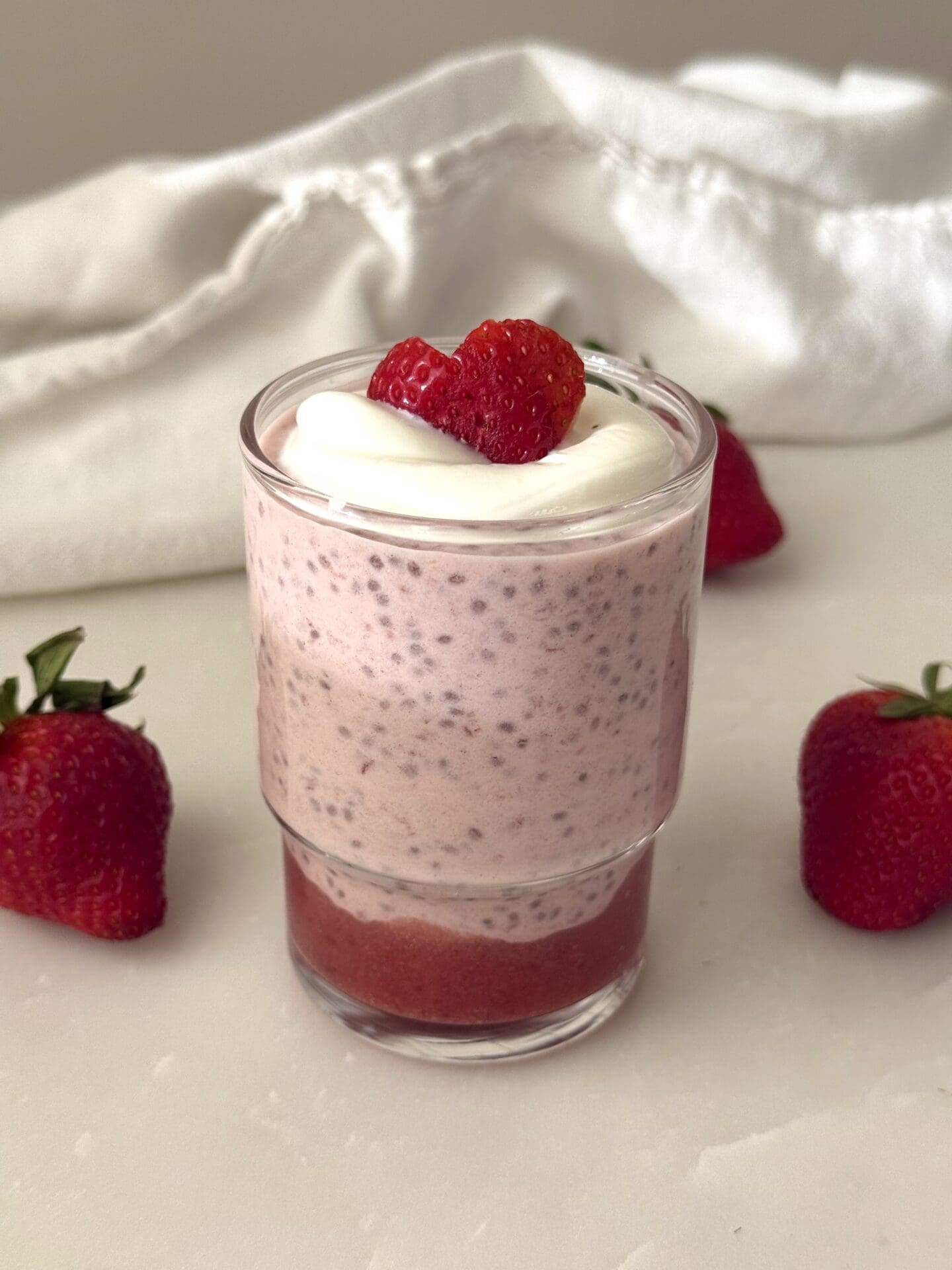 IMG_4159 A single serving of strawberry chia seed pudding sits on a white marble table surrounded by fresh strawberries.