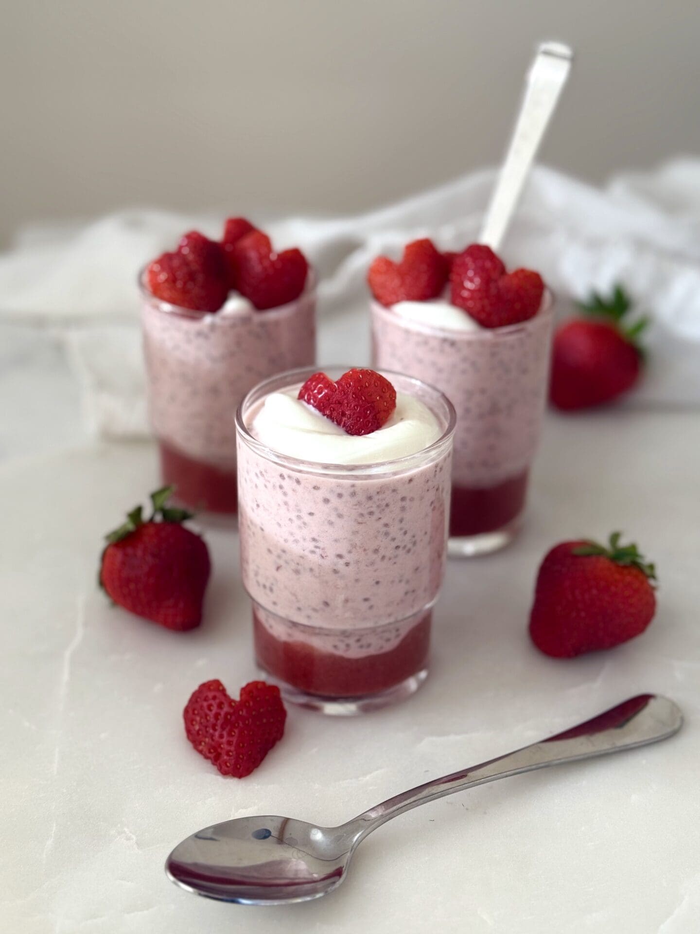 IMG_4171 A trio of glass jars hold individual servings of strawberry chia seed pudding. The puddings are garnished with heart shaped strawberry slices.