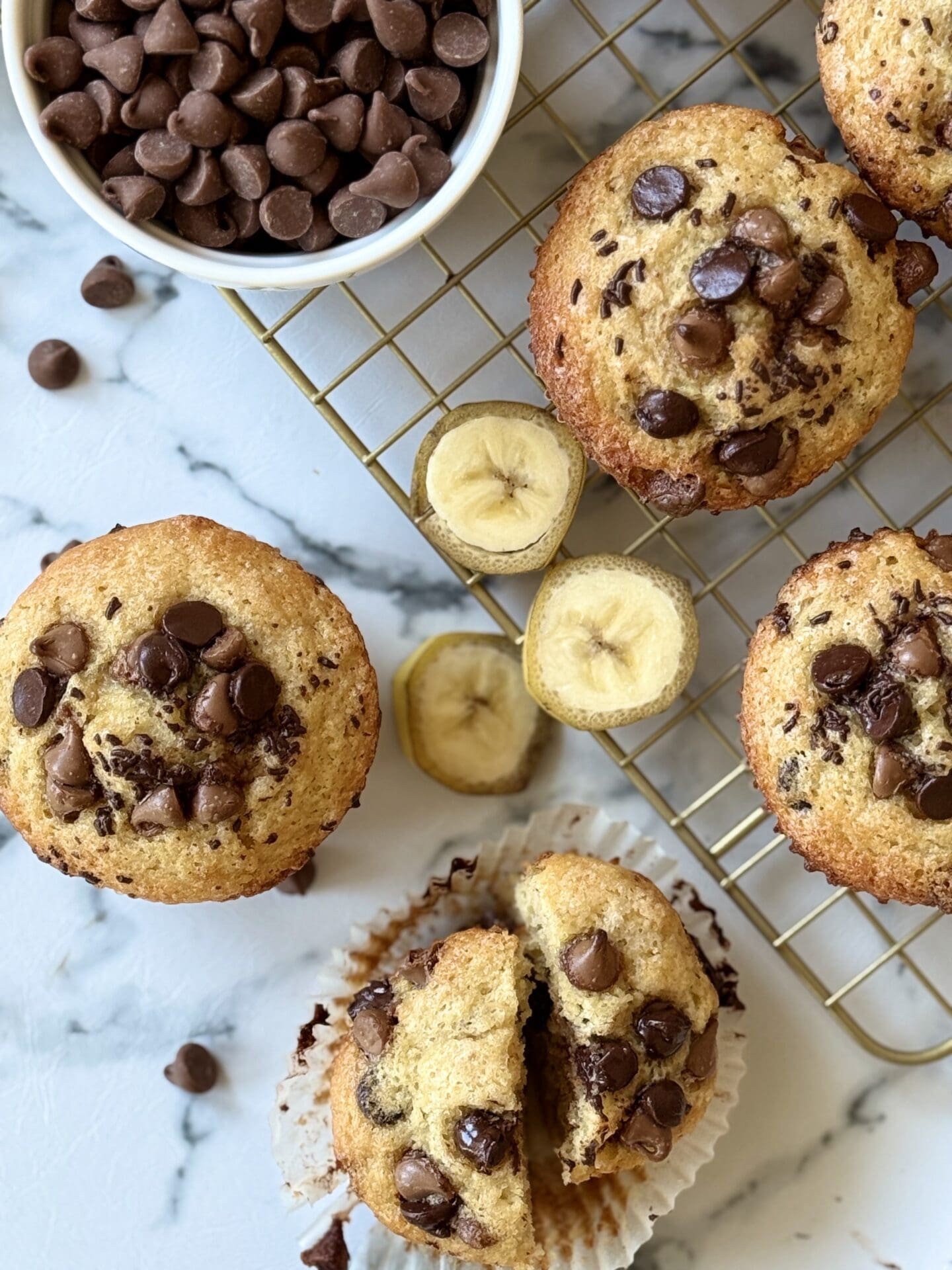 IMG_4517 Four Sour Cream Banana Chocolate Chip Muffins are seen from above, surrounded by slices of fresh bananas and chocolate chips.