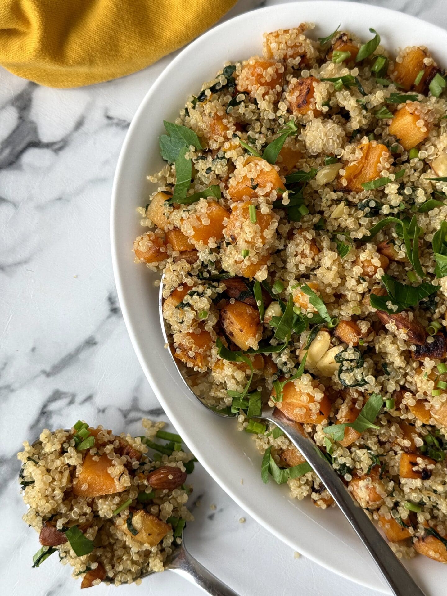IMG_4704 Half of a serving platter full of quinoa salad with butternut squash, spinach and crunchy almonds is seen on white marble counter. A serving spoon overflowing with the salad sits beside the platter.