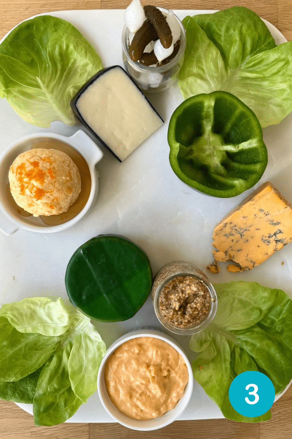 45E17EEB-CEA6-4C4A-85B8-7EC76B522281 Step 3 in building a St Patrick's Day Charcuterie Board. Dishes of pickles and grainy mustard are added to the board.