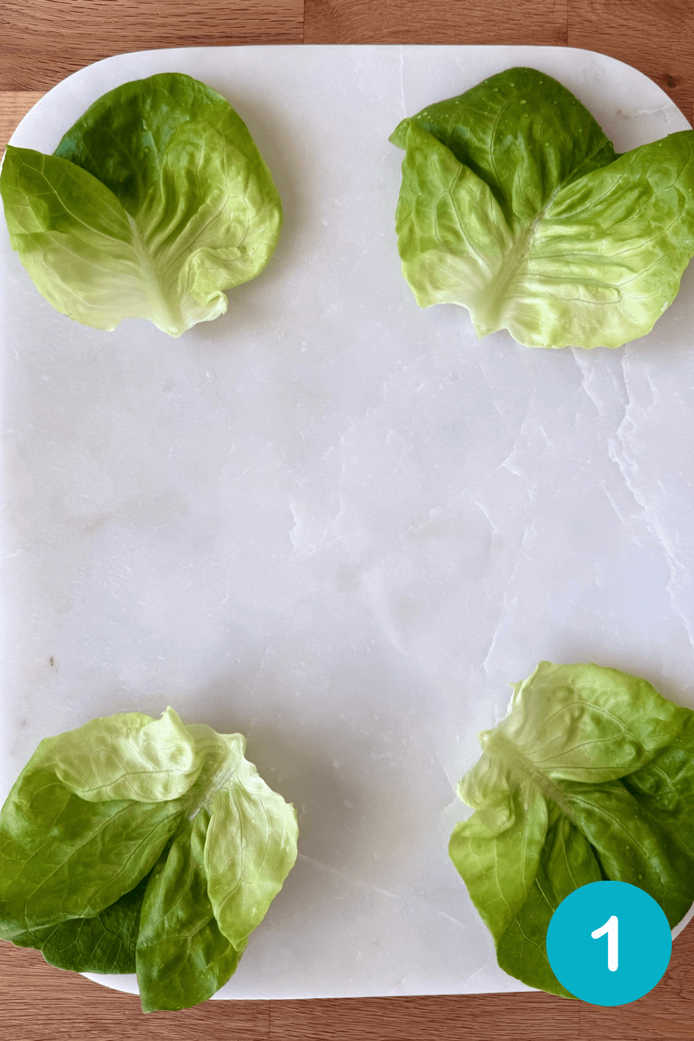 D37D400C-E209-4CC9-A7F4-3772968058BB Step 1 of building a St Patrick's Day Charcuterie Board. Large green lettuce leaves have been placed on a white marble cheese board.