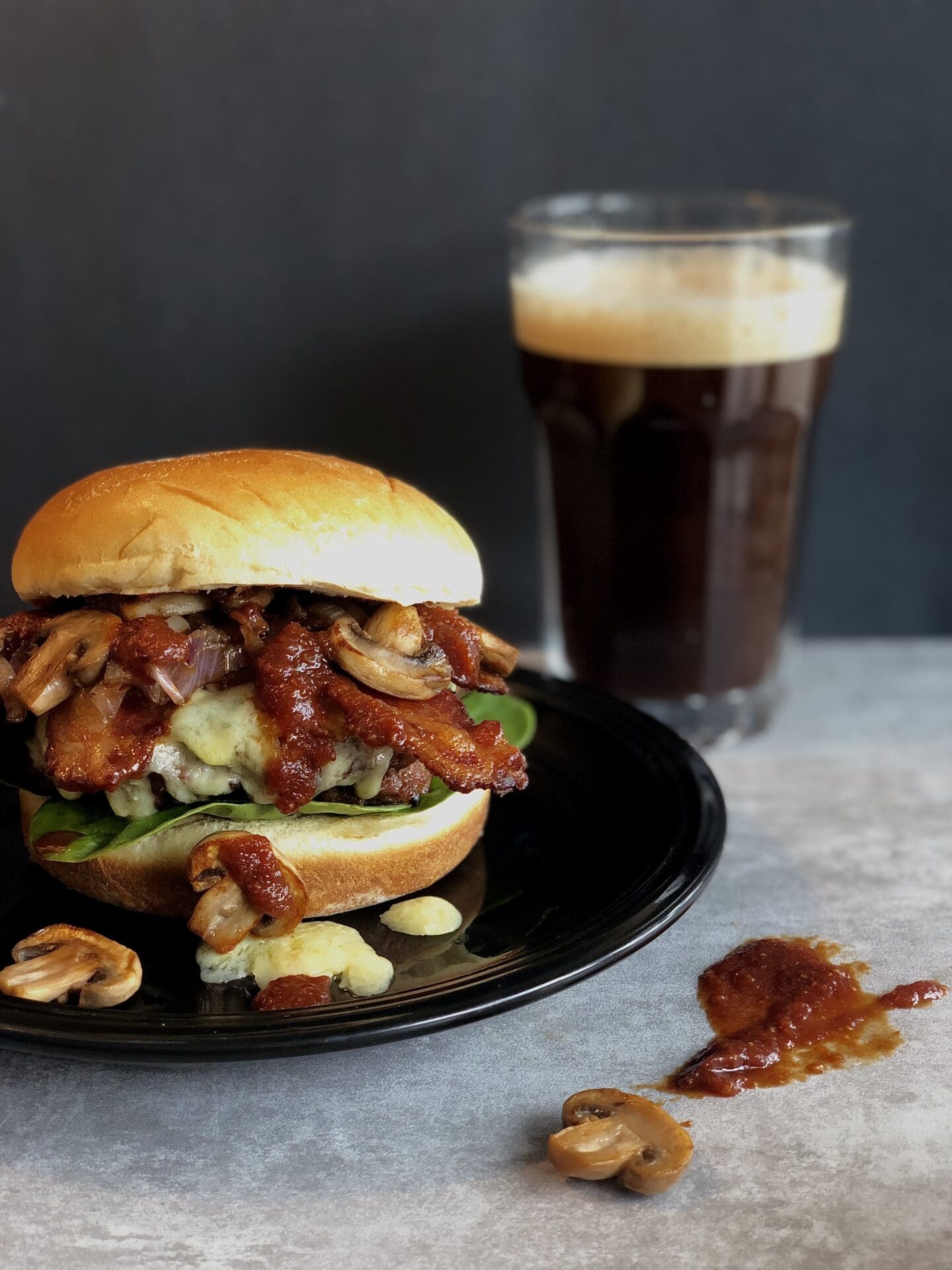 IMG_4189 A Guinness Bacon Burger with Mushrooms and Irish Cheddar is seen on the left side of the photo. A pint of Guinness beer and a drip of homemade Guinness barbecue sauce can be seen on the right.