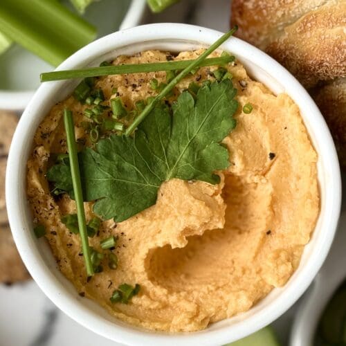 A dish of orange Pub Style Beer Cheese is seen from above, in close up, garnished with fresh green herbs.