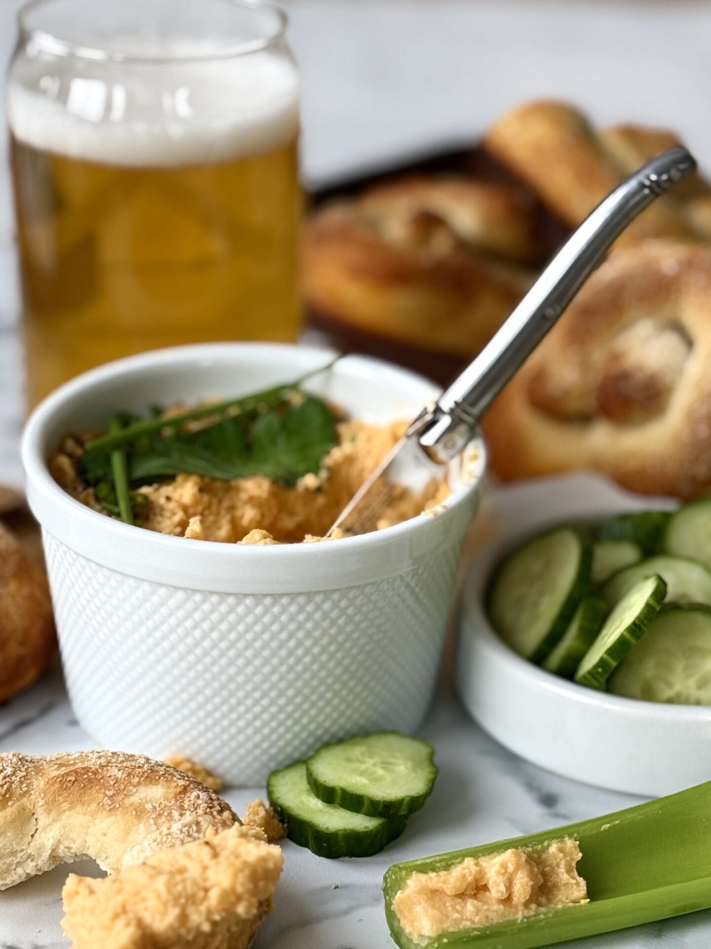 IMG_4650 A bowl of Creamy Pub Style Beer Cheese Dip is seen surrounded by a cold beer, vegetables and soft pretzels.