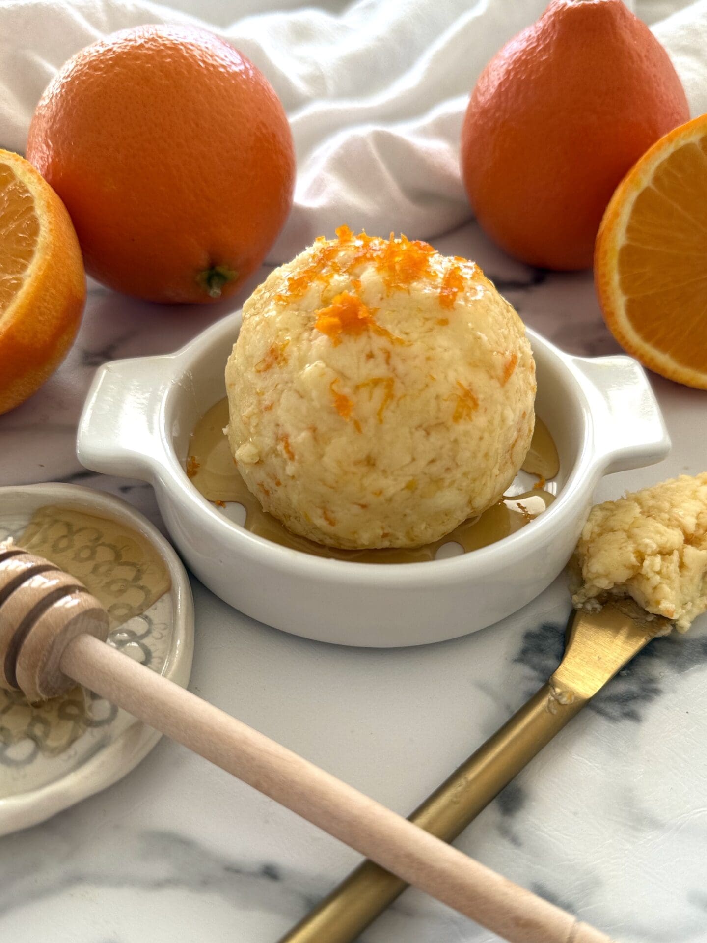 IMG_4797 Orange and Honey Butter is shaped into a ball, placed in a shallow butter dish, drizzled with extra honey and garnished with fresh orange zest. Fresh oranges and a honey dipper complete the image.