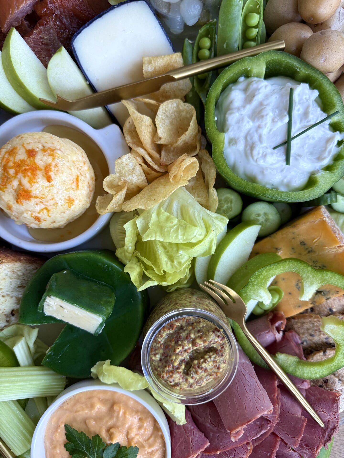 A St Patrick's Day Charcuterie Board is seen close up, from above.  The board features green vegetables, oranges cheeses and white dip, representing the colours of the Irish flag.